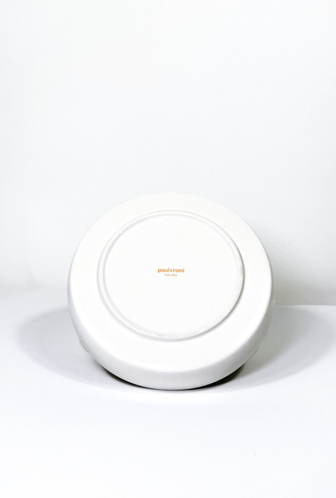 Bottom view of white Vela Alba pasta plate with orange paul & romi logo
