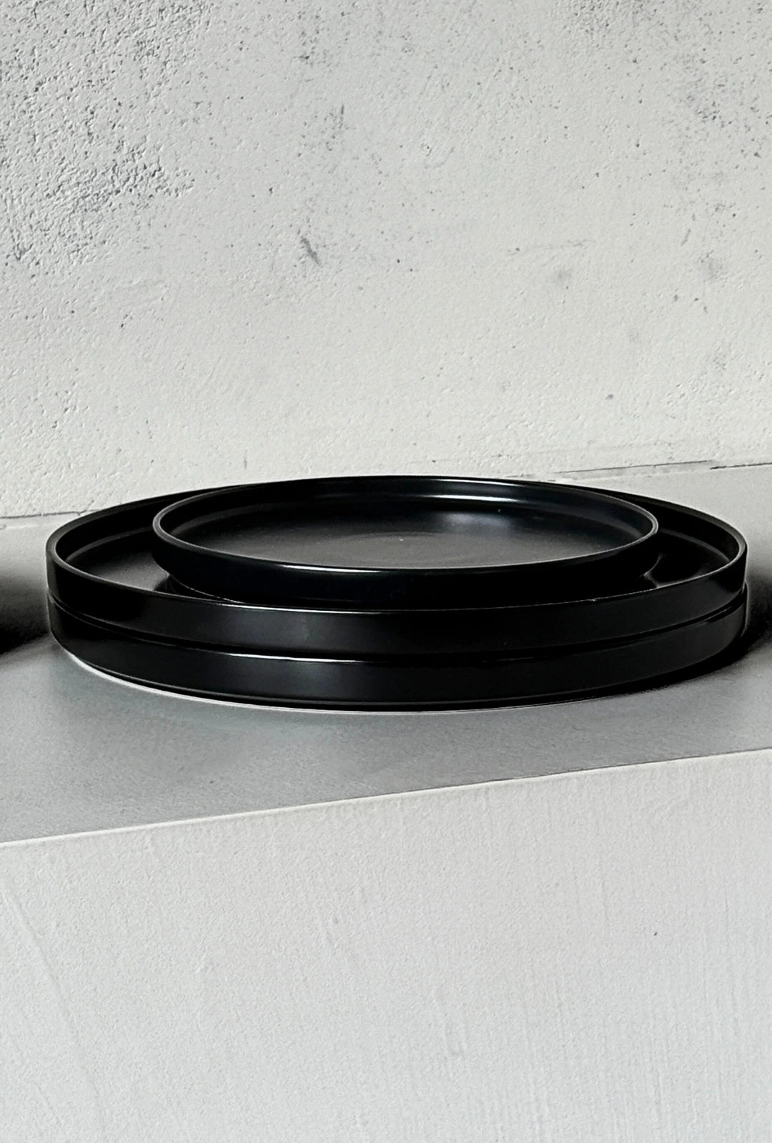 Close up of nested black rimmed plates from the Vela Luna 40 piece dinnerware set on a light textured surface