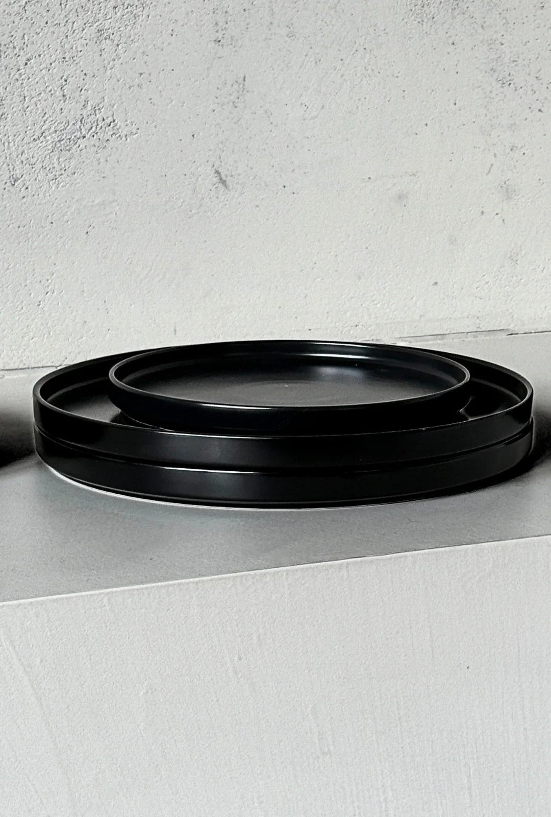 Close up of nested black rimmed plates from the Vela Luna 40 piece dinnerware set on a light textured surface