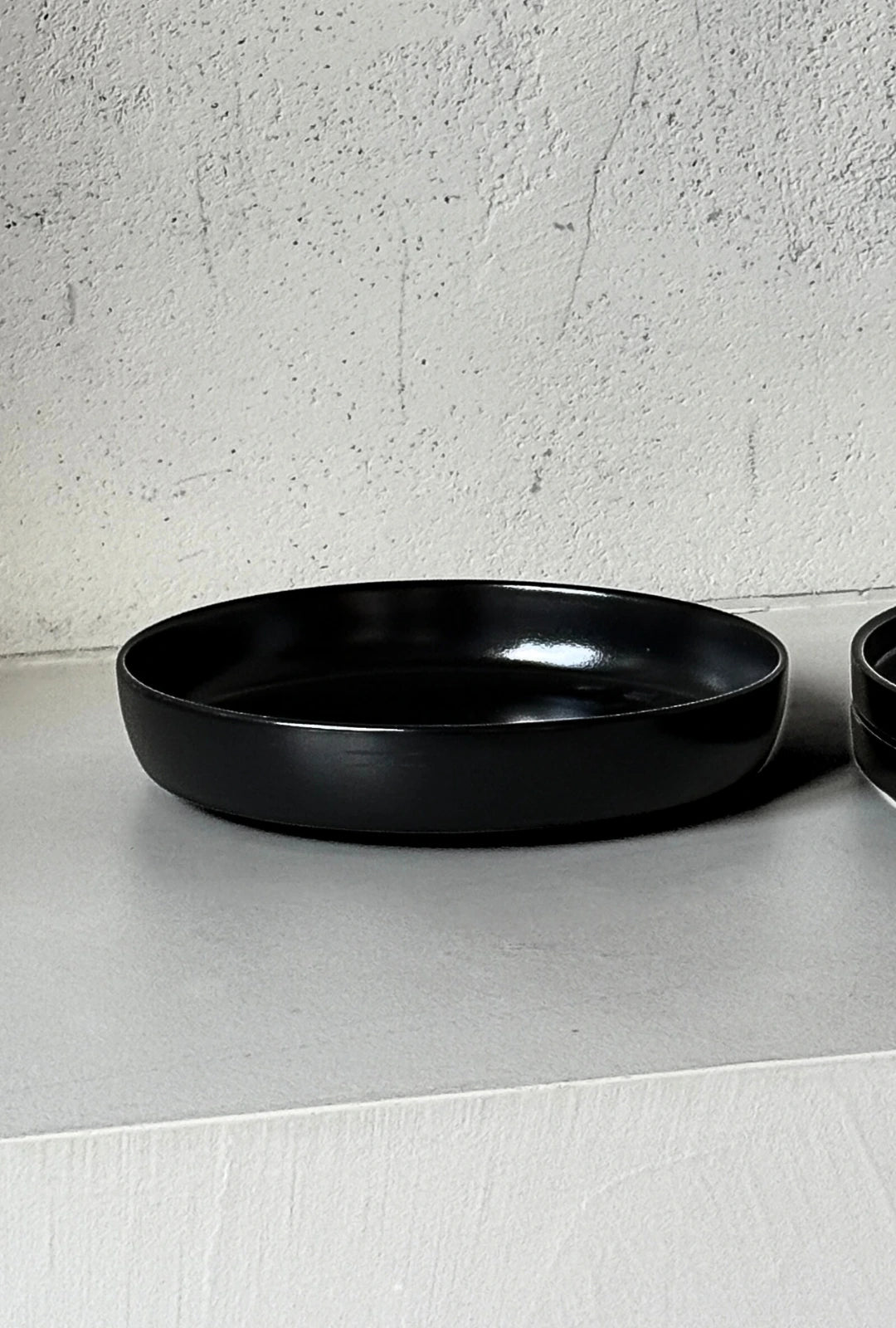 Black circular dishes from the Vela Luna set arranged on a light surface against a textured white wall