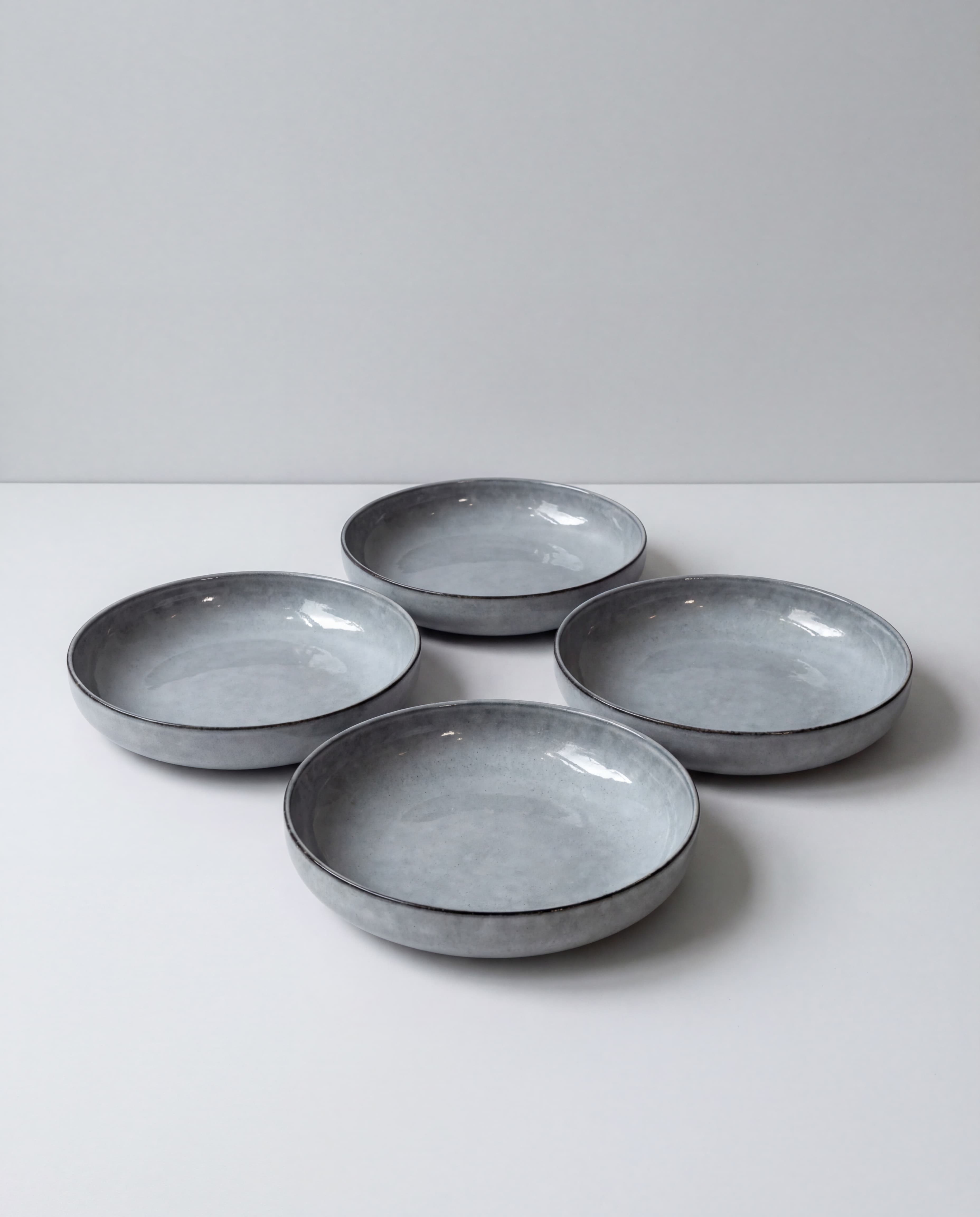 Group of shallow grey ceramic bowls arranged on a white table against a pale grey backdrop