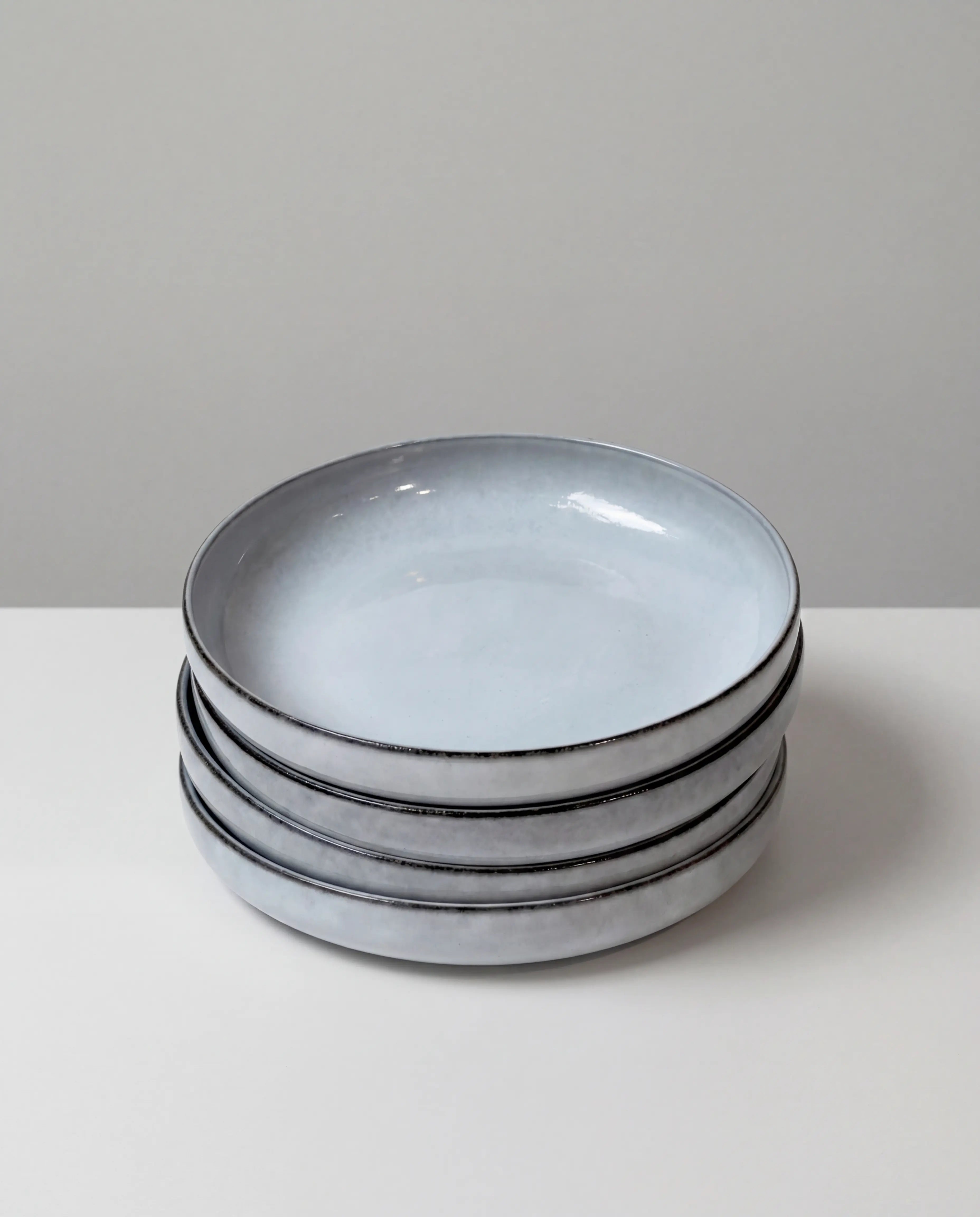 Stack of six Nordic Fjord pasta bowls with white rims and blue gray interiors.