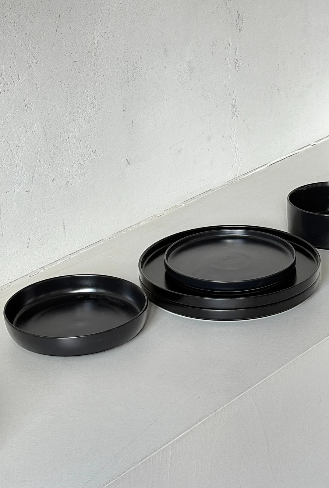 Vela Luna 40 piece black dinnerware set arranged on a light surface with stacked plates and bowls