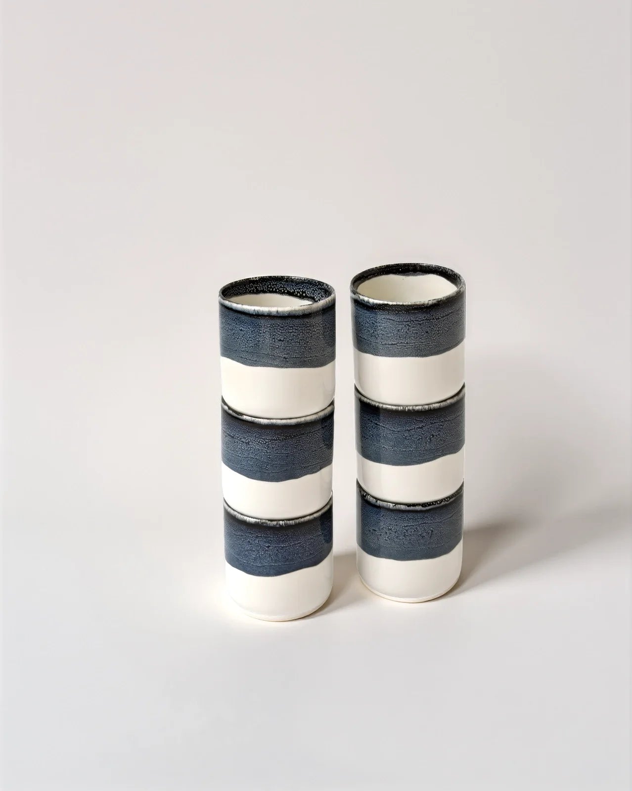 Two cylindrical cups with navy blue glaze and white middle band placed side by side.