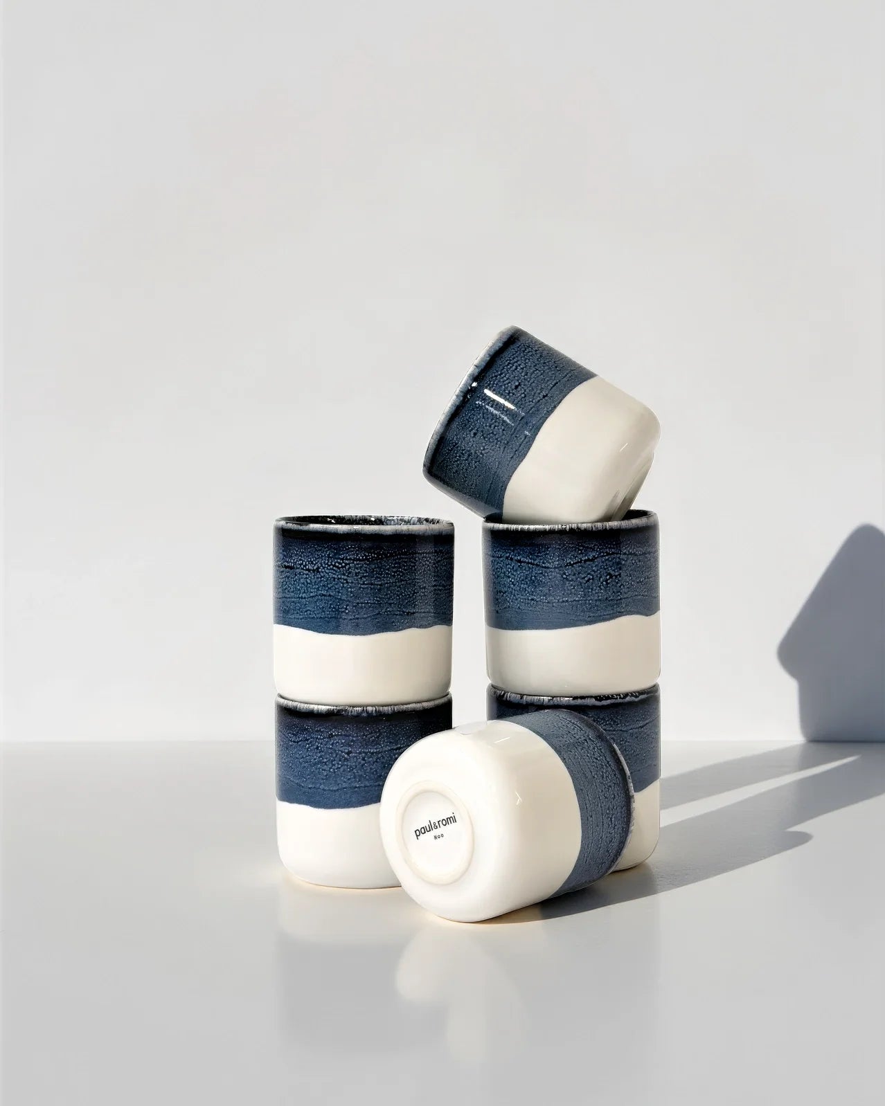 Stack of blue and white glazed cups from Noa Kaffeemomente Set, one cup balanced on top.