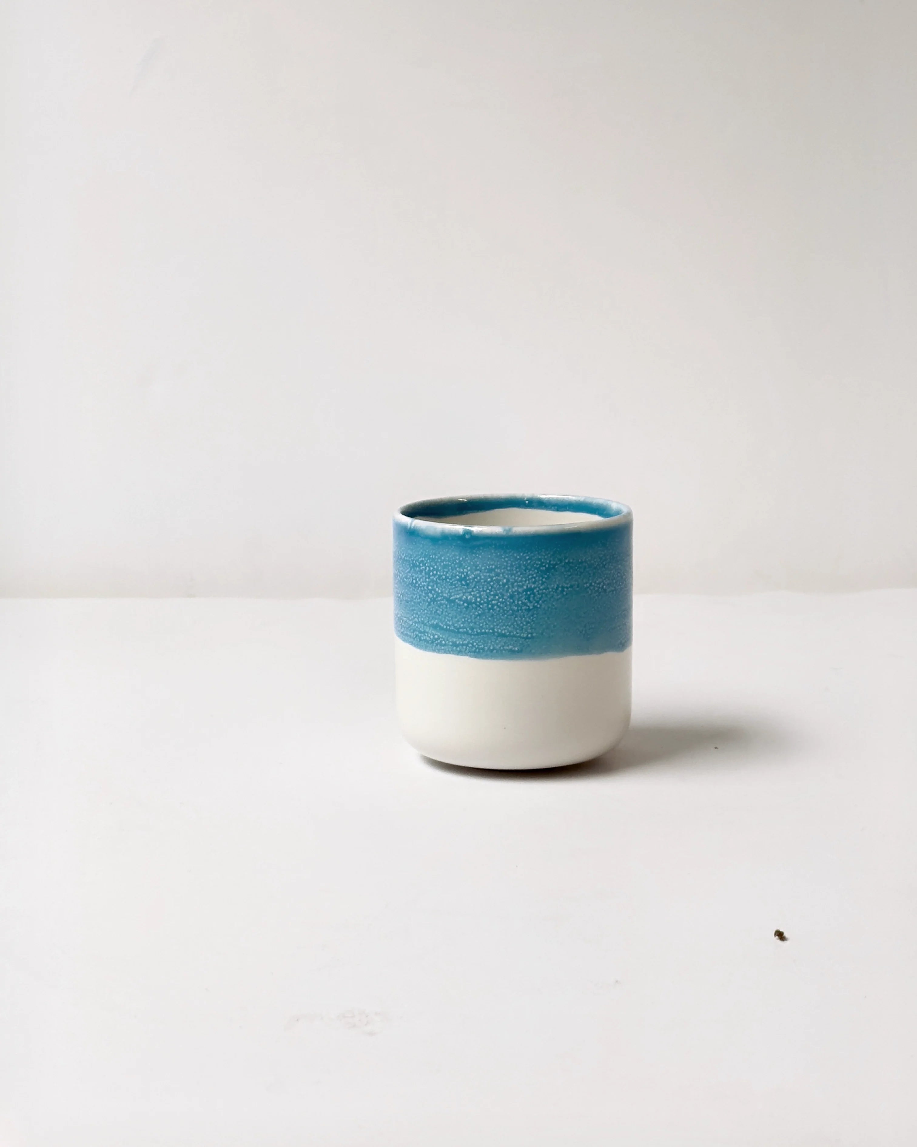 Blue glazed ceramic cup with turquoise rim on a white background, part of the Kaffeemomente Set.