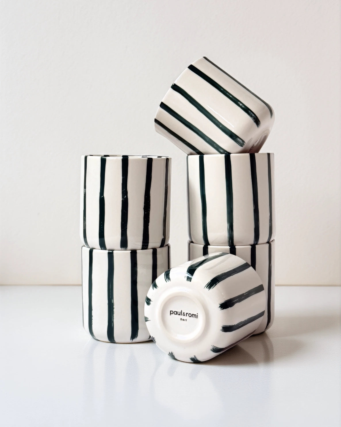 Stacked striped Karl mugs with a tilted cup and a base showing paul & romi Karl.