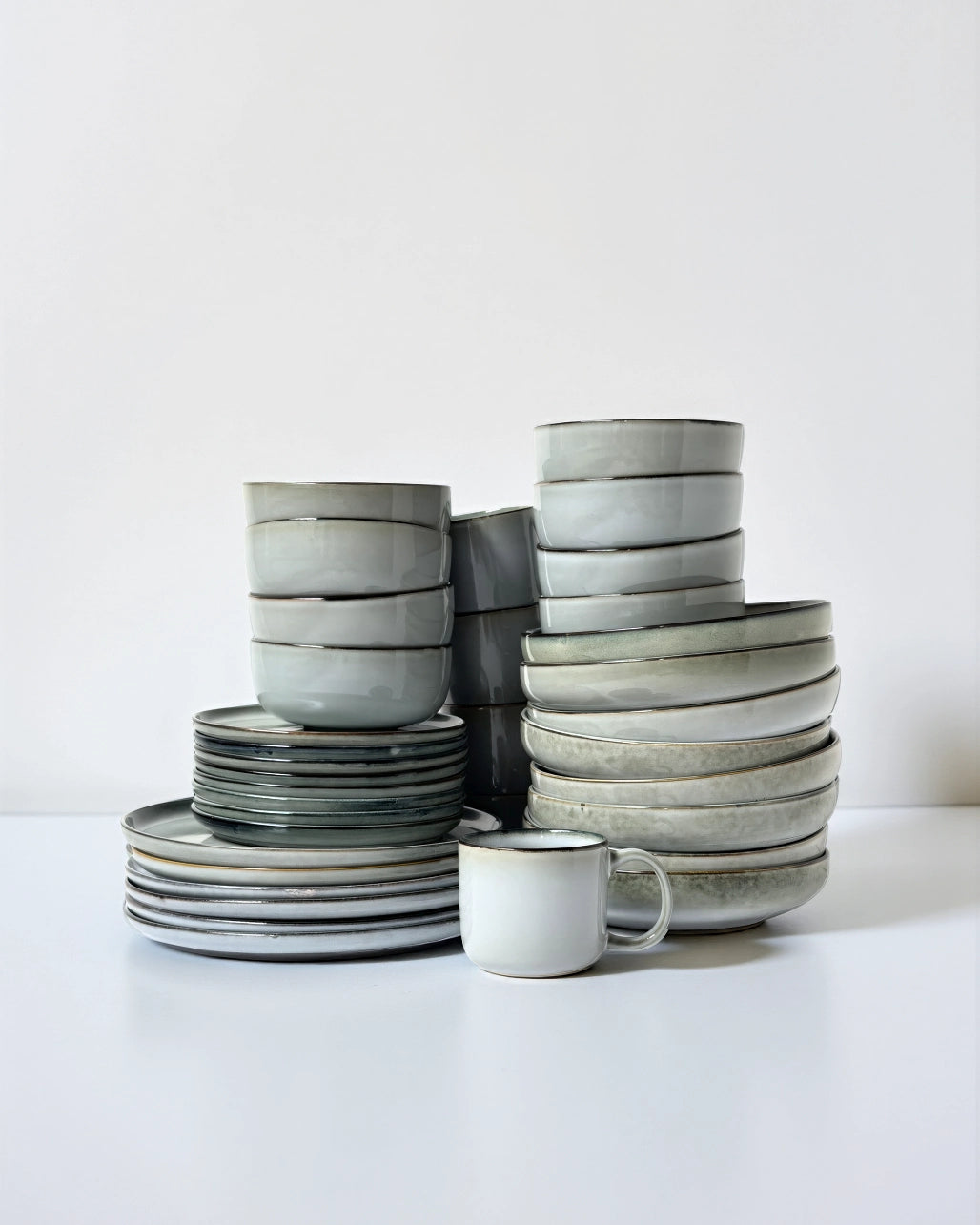 Stack of Scandic Soul Nordic Forest dinnerware bowls and plates with a mug in muted gray glaze