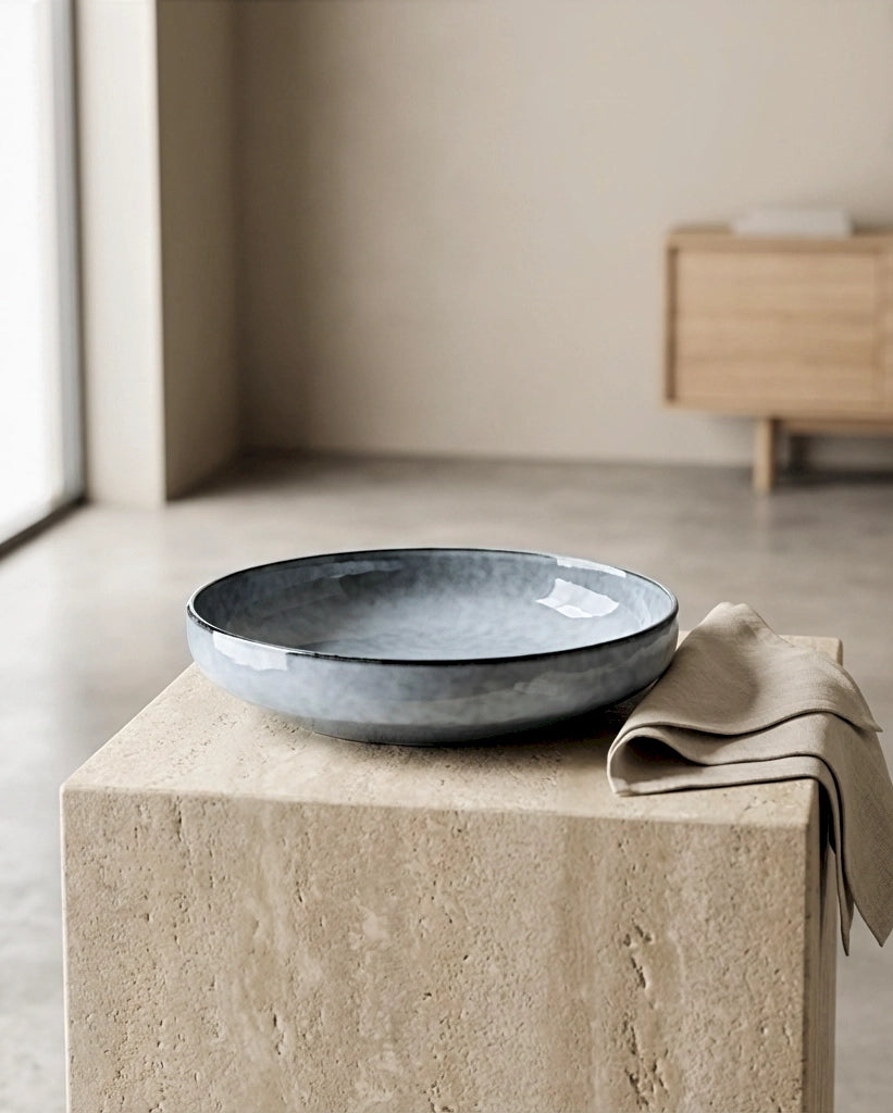 Blue grey Nordic Fjord pasta plate resting on a beige stone pedestal with a folded napkin