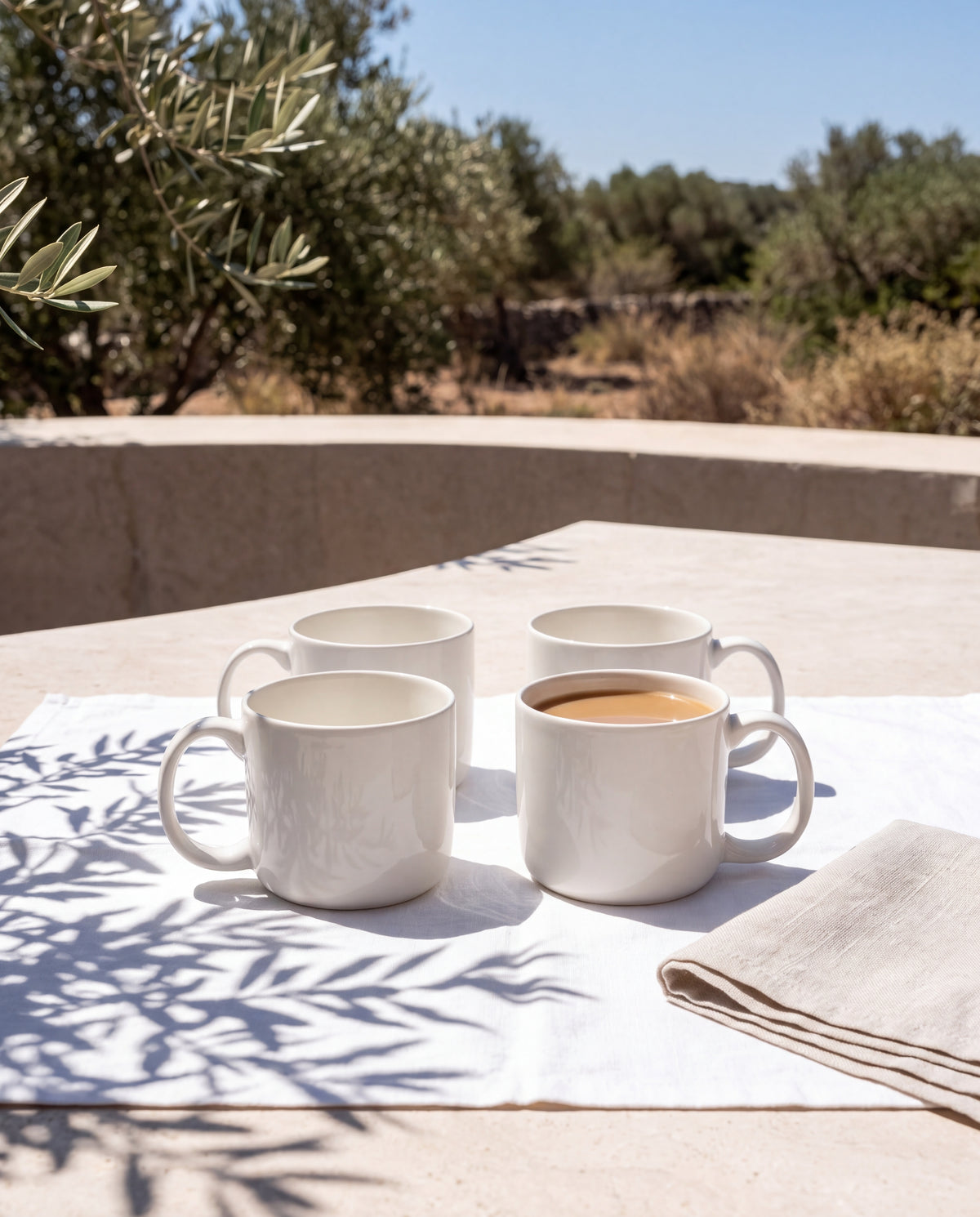 Vier weiße Vela Alba Tassen auf Leinen, eine mit Milchkaffee