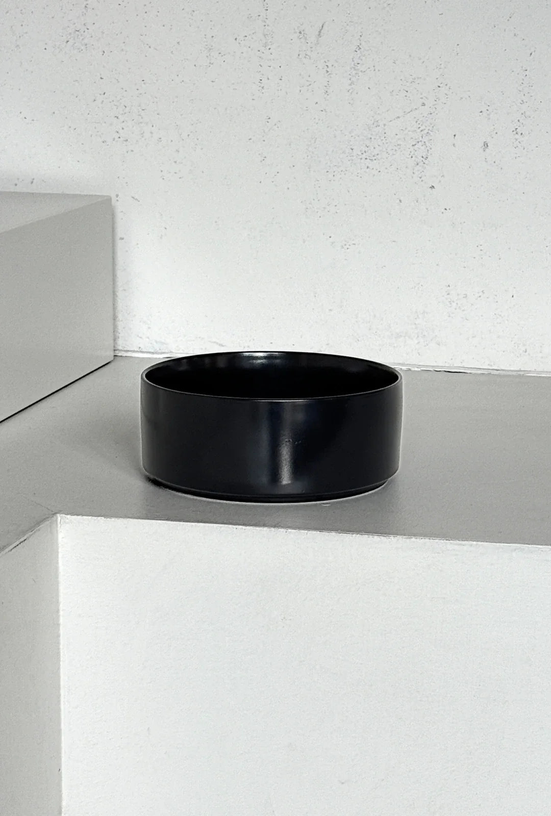 Vela Luna 32 piece black dinnerware set a single round black bowl on a light shelf