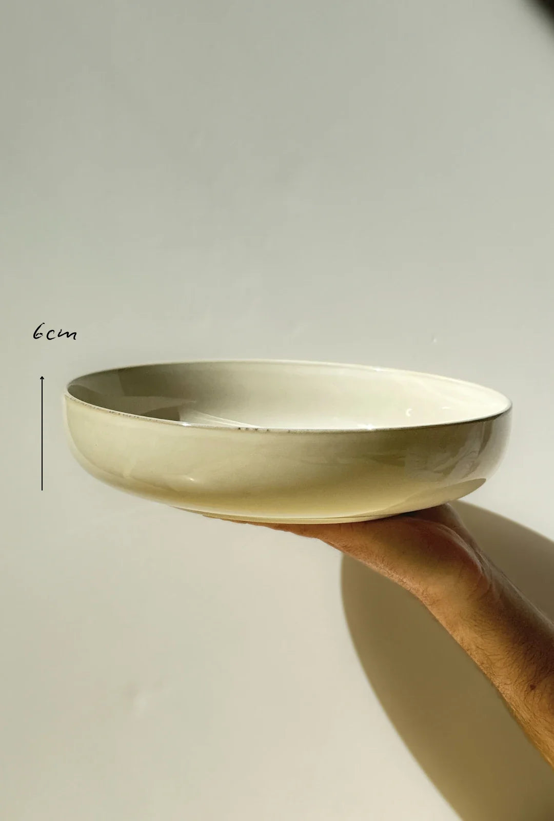 Hand holds a small shallow beige ceramic bowl from the Scandic Sails 40 piece set showing 6 cm height