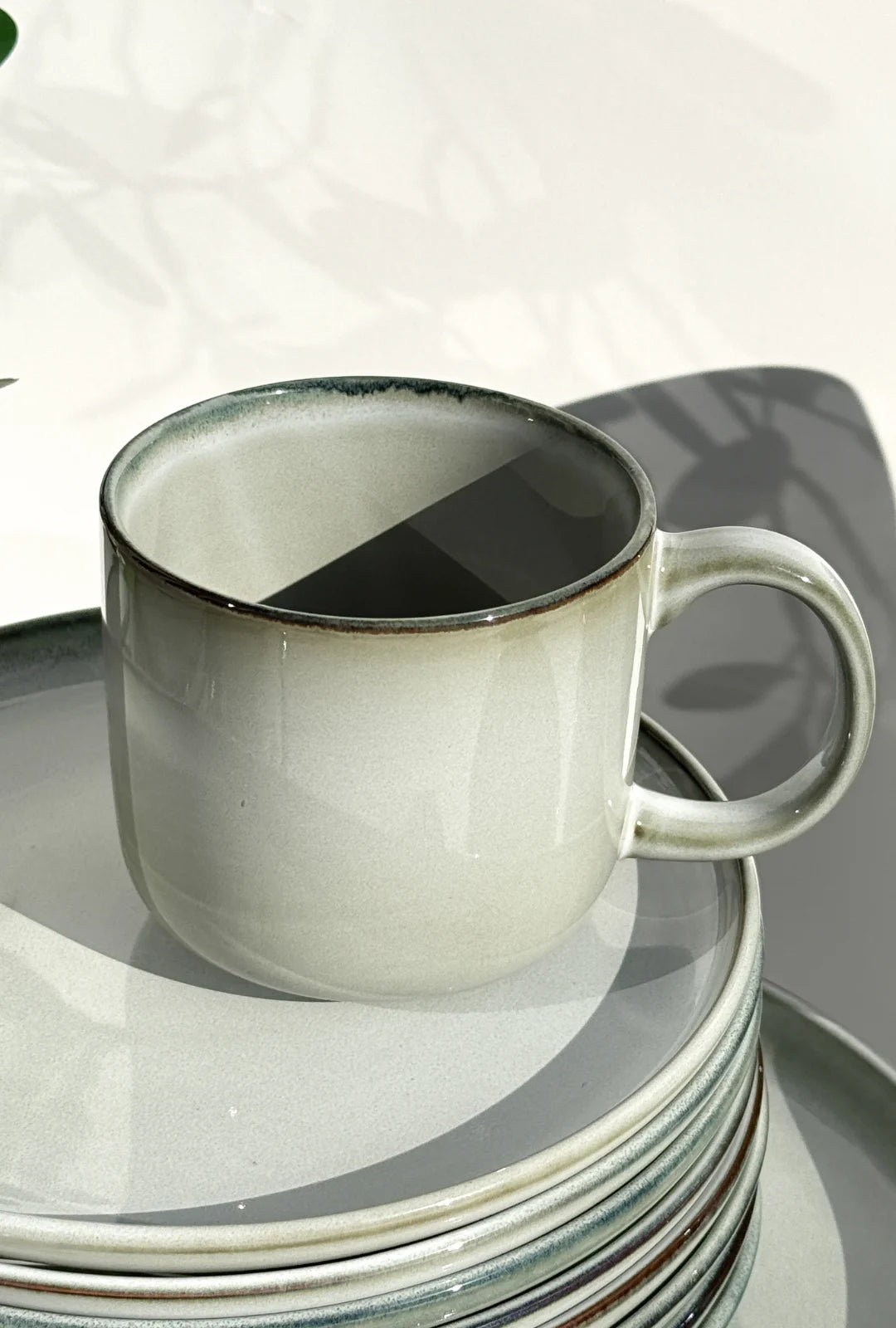Scandic Soul Nordic Forest mug in pale gray with a dark rim atop a stack of plates.