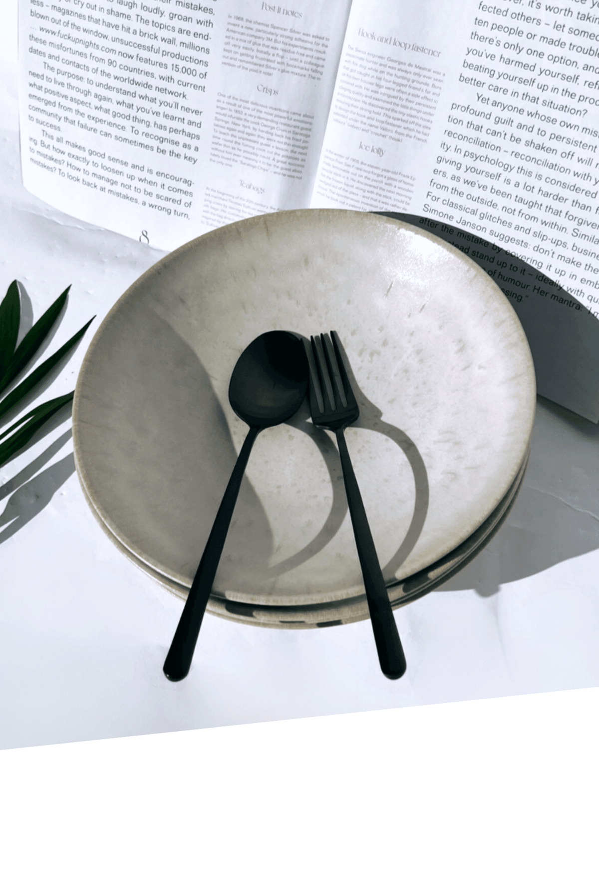 Bom Dia pasta plate with matte black spoon and fork on a white surface with printed pages in the background.