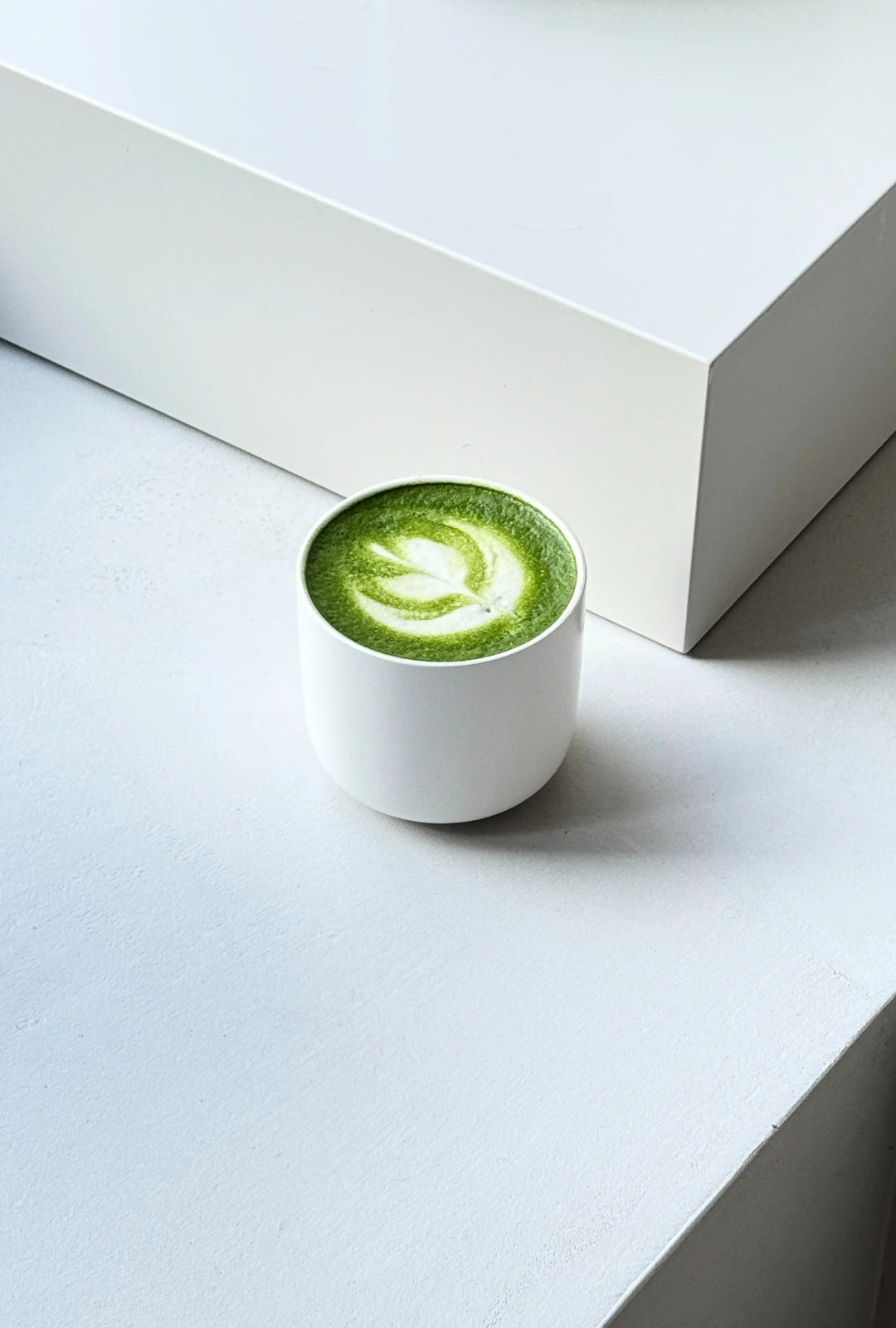 White Vela Alba cup on a white surface with a green matcha latte and latte art