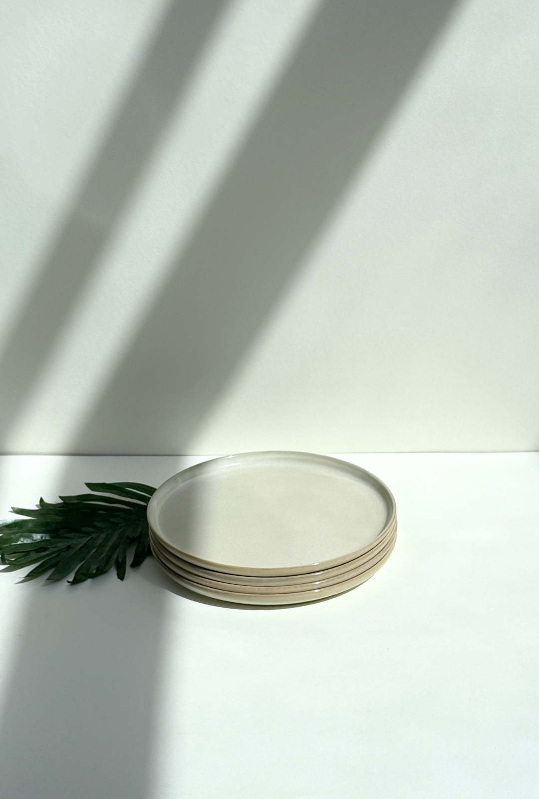Stack of Scandic Sails large cream plates with tan rims on a white surface with a pale wall and diagonal shadows