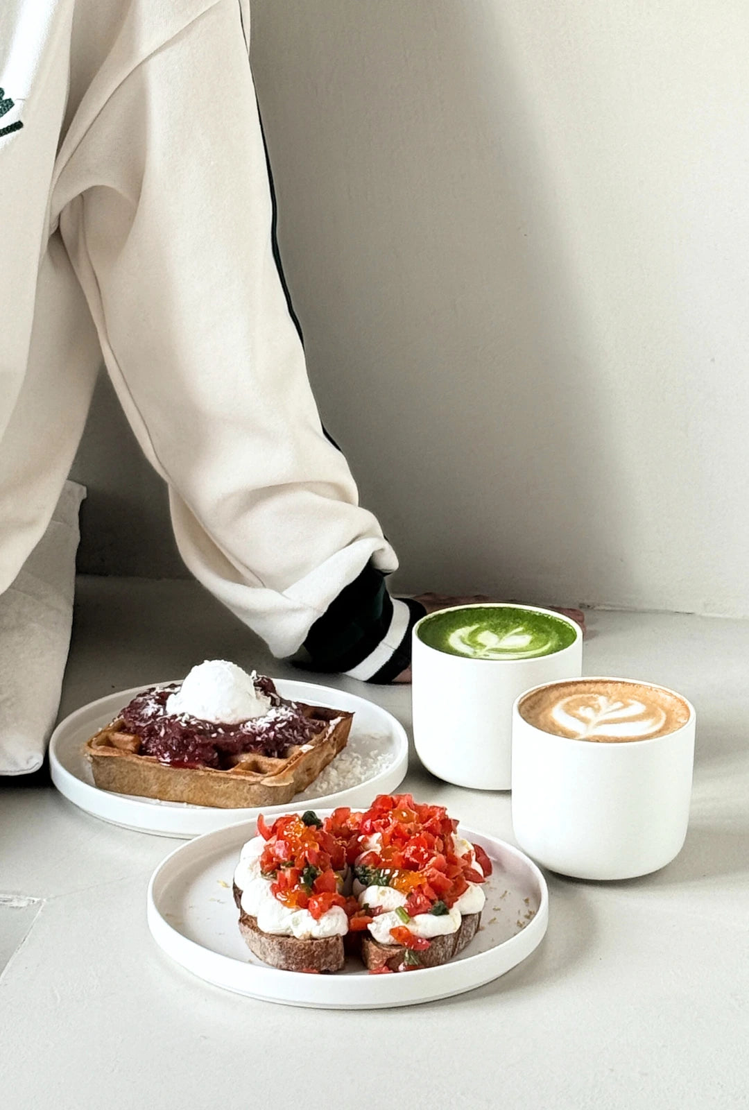 Vela Alba small plate setting with a green matcha latte and a cappuccino beside a berry pastry on a light table