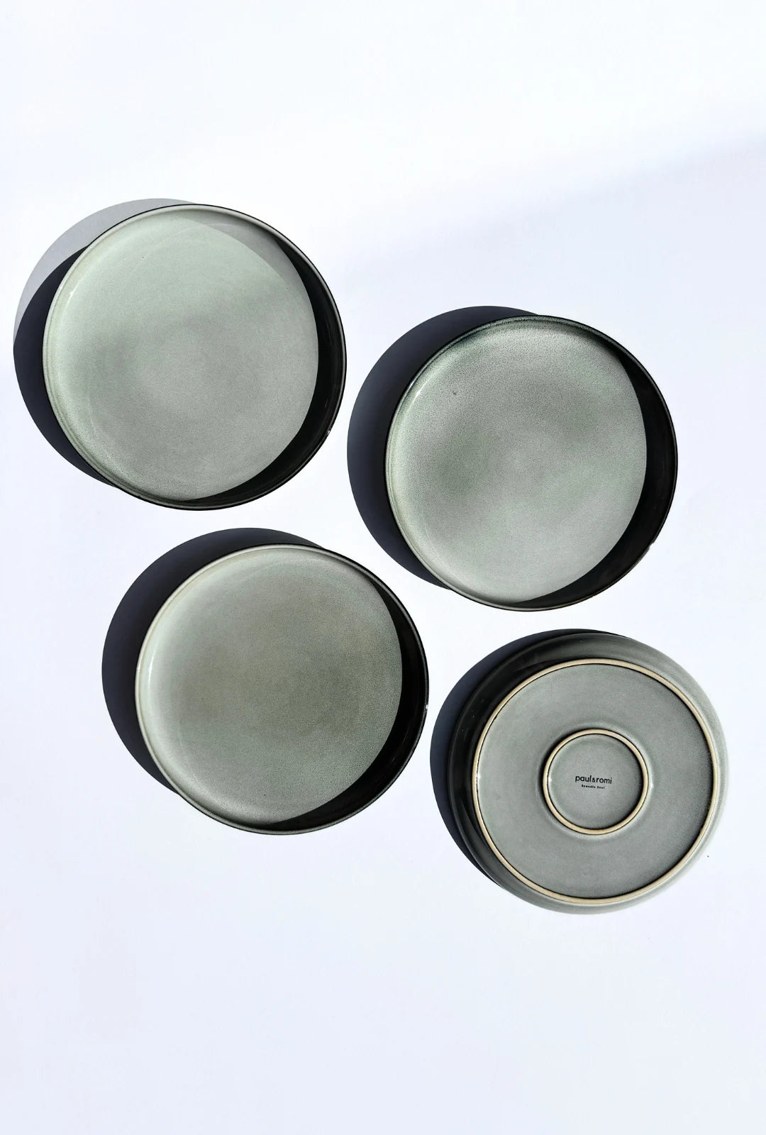 Top down view of four Nordic Forest plates with pale gray glaze and a branded bottom plate.