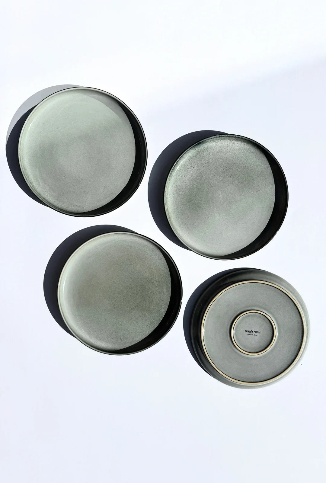 Top down view of four Nordic Forest plates with pale gray glaze and a branded bottom plate.