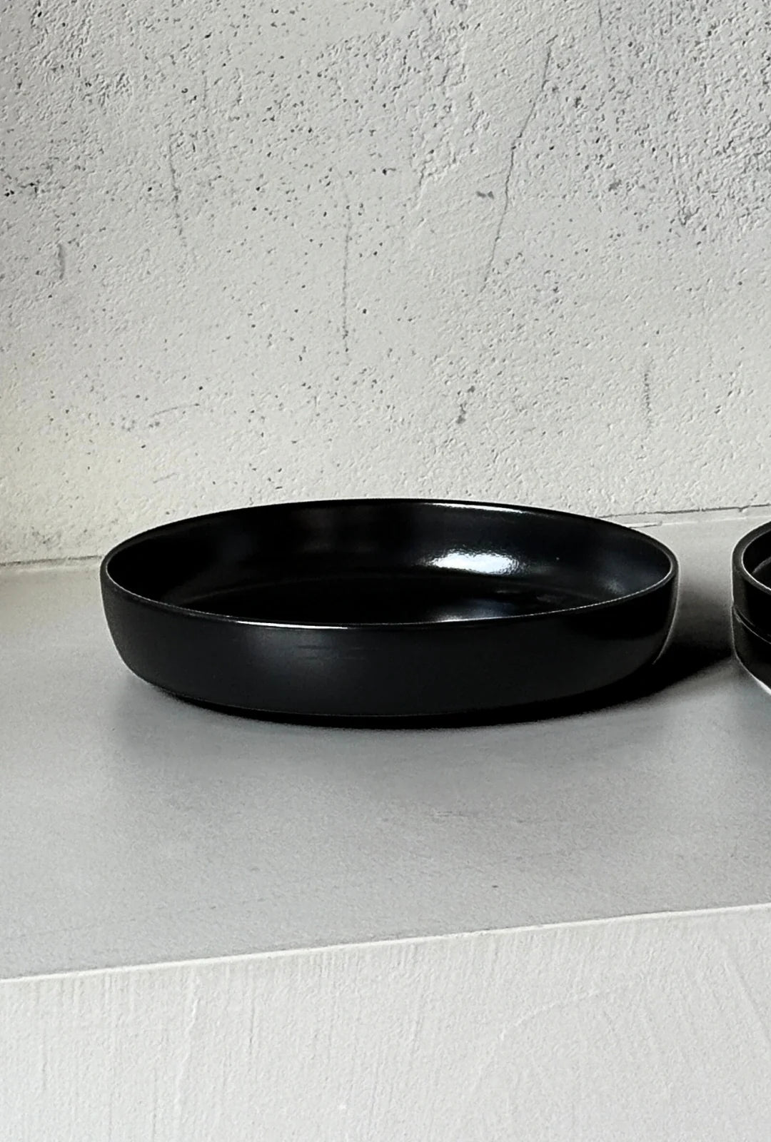 Black circular dishes from the Vela Luna set arranged on a light surface against a textured white wall