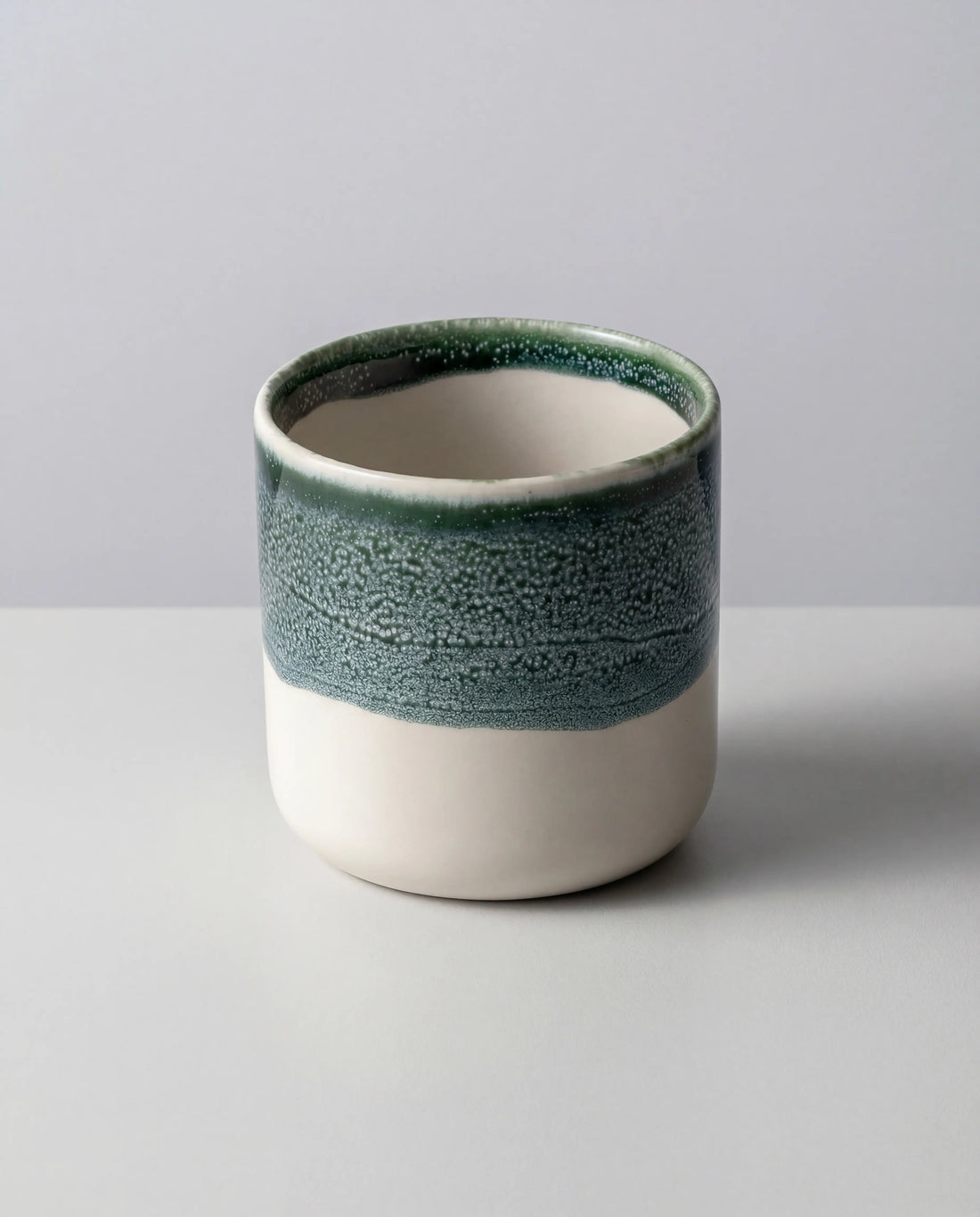 Close-up of a Becher Tilde mug showing a blue green glaze around the rim and white interior.