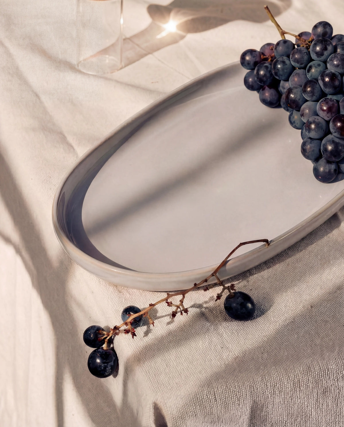 Grapes resting on a Lyra four piece serving plate set displayed on linen backdrop