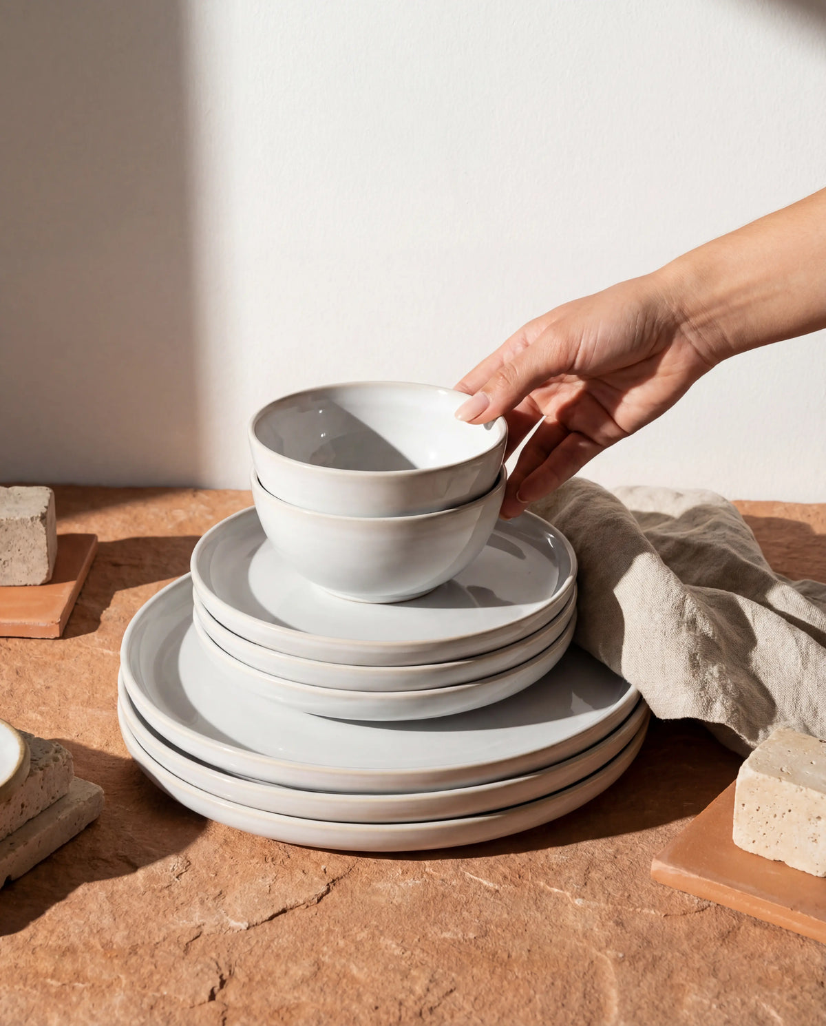 Hand stacking white ceramic bowls from Lyra 16 piece dinnerware on a wooden surface