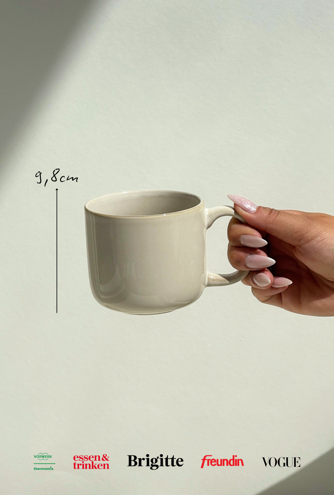 Beige ceramic Scandic Sails mug held by a hand with long pink nails against a pale wall