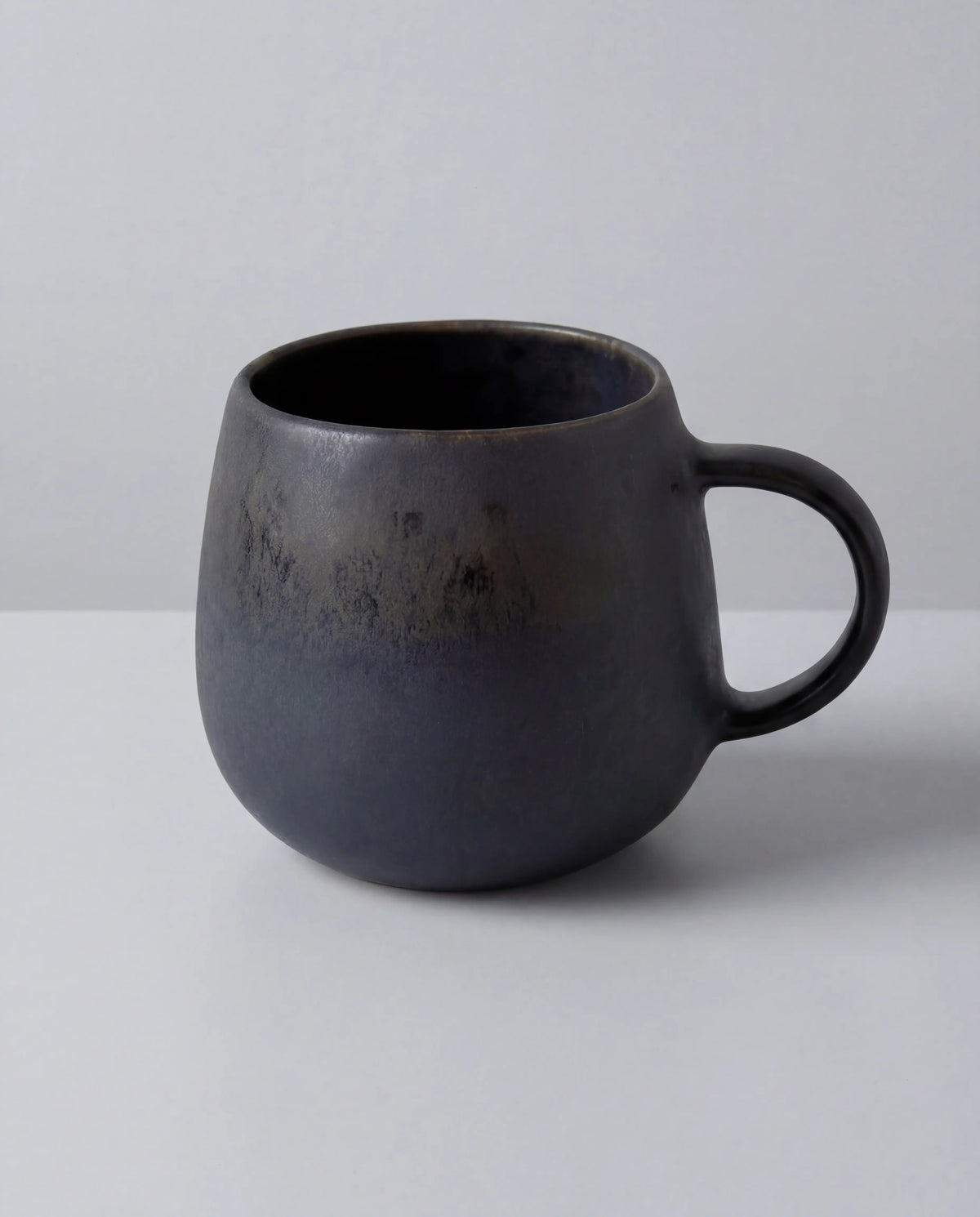 Close-up of a dark Alfama Tasse mug showing its rounded form and lip against a light background.