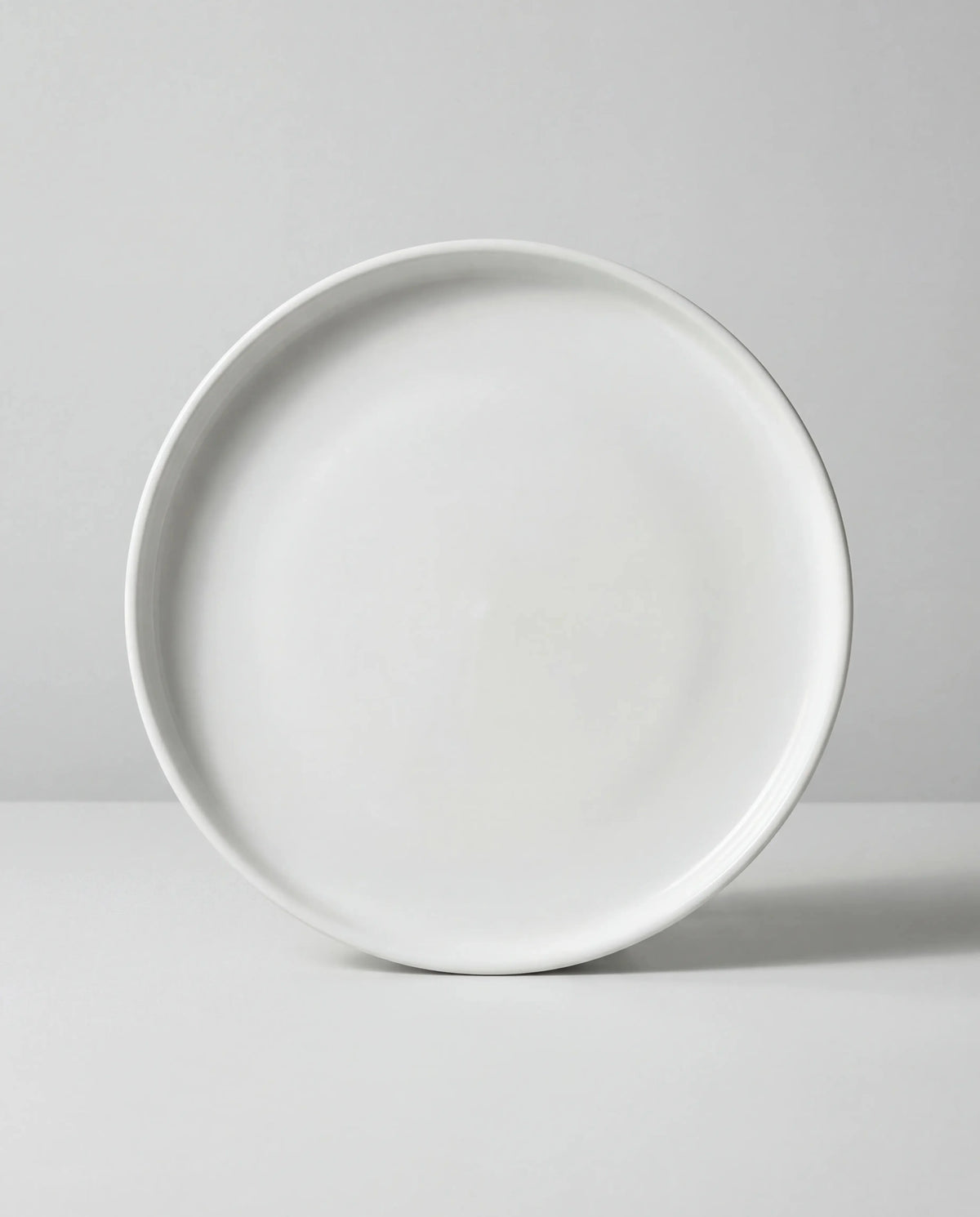 Close up of a white round plate edge against a light gray background.