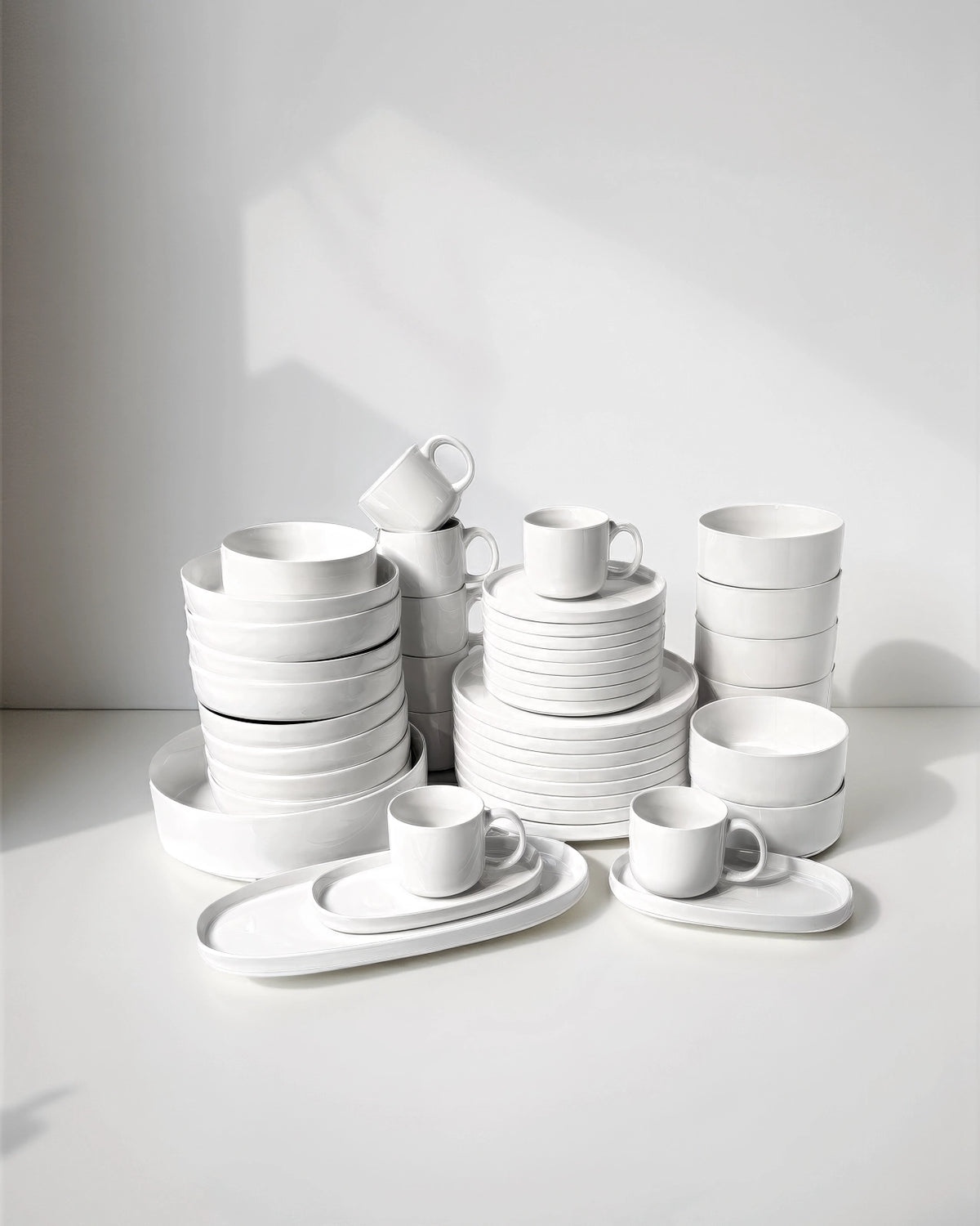 Stacked white Vela Alba dinnerware including bowls plates and cups on a clean surface