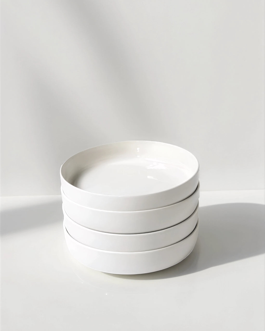 Stacked white pasta bowls on a white surface with a soft grey backdrop