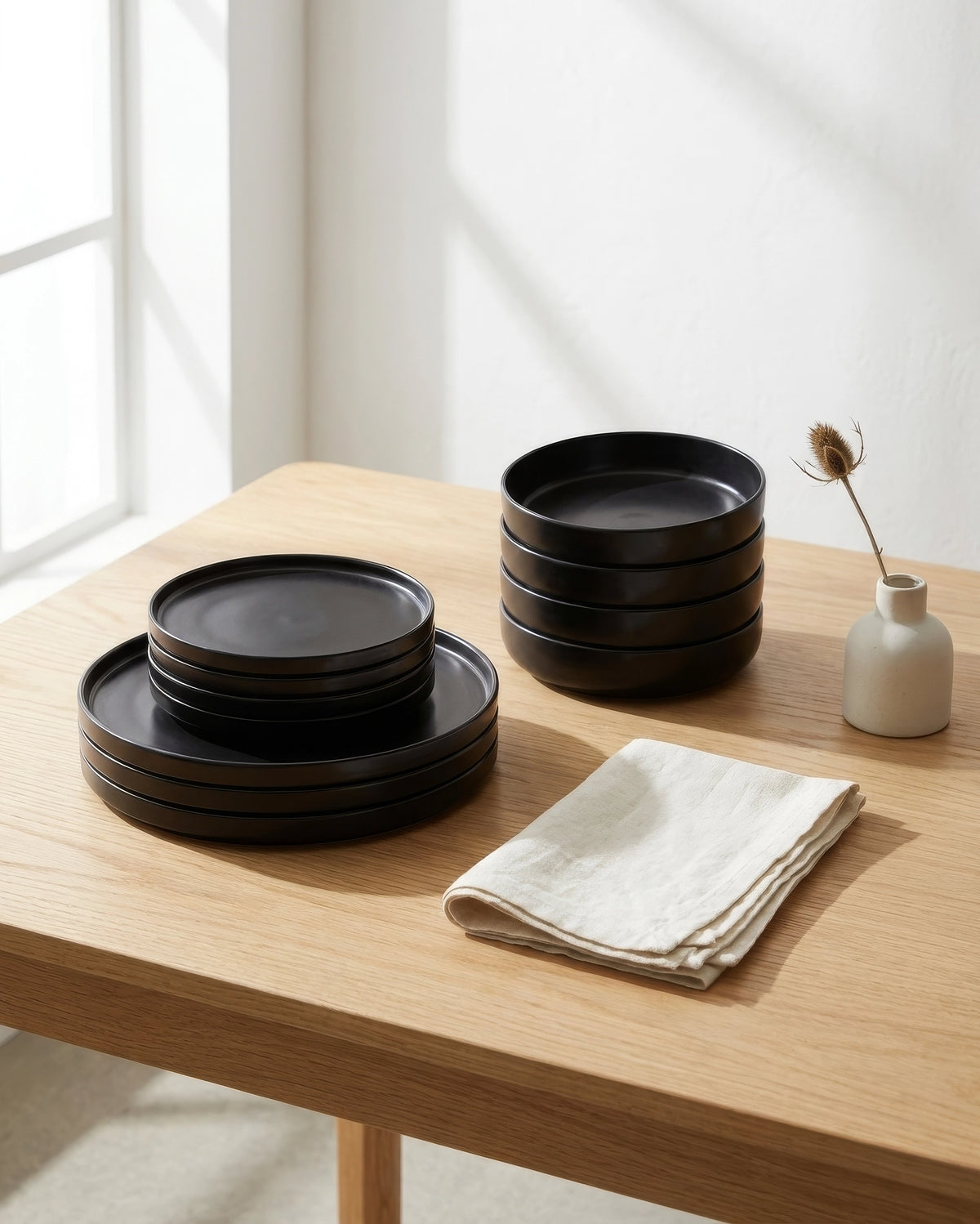 Vela Luna black bowls on a wooden table with a beige vase and dried flower