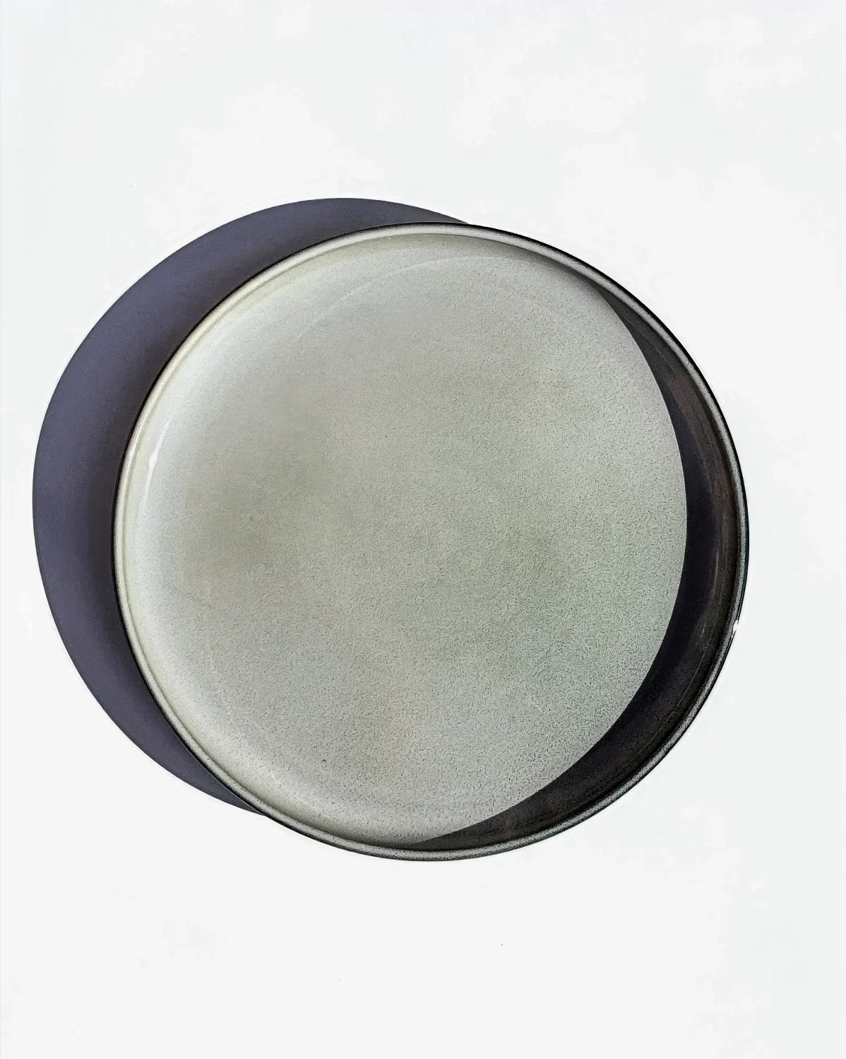 Top view of a light grey speckled Nordic Forest small plate stacked on a larger dark blue plate