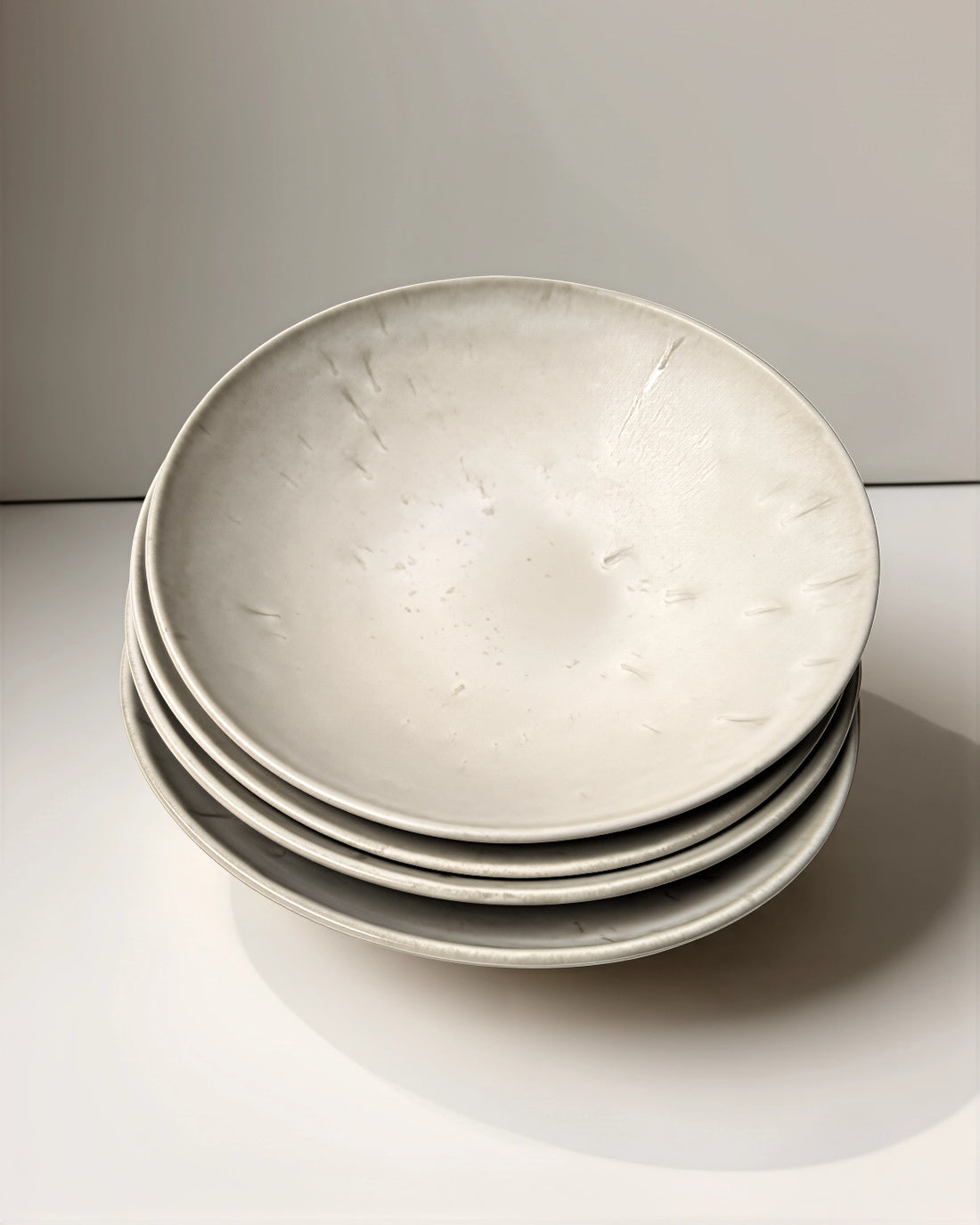 Stack of four round Bom Dia Pastateller ceramic plates in soft grey with a speckled glaze