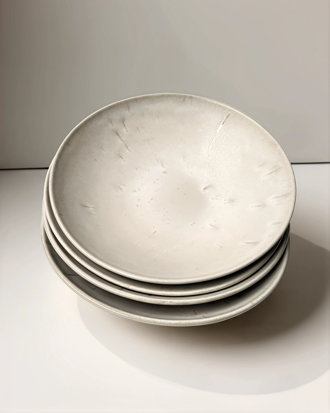 Stack of four round Bom Dia Pastateller ceramic plates in soft grey with a speckled glaze
