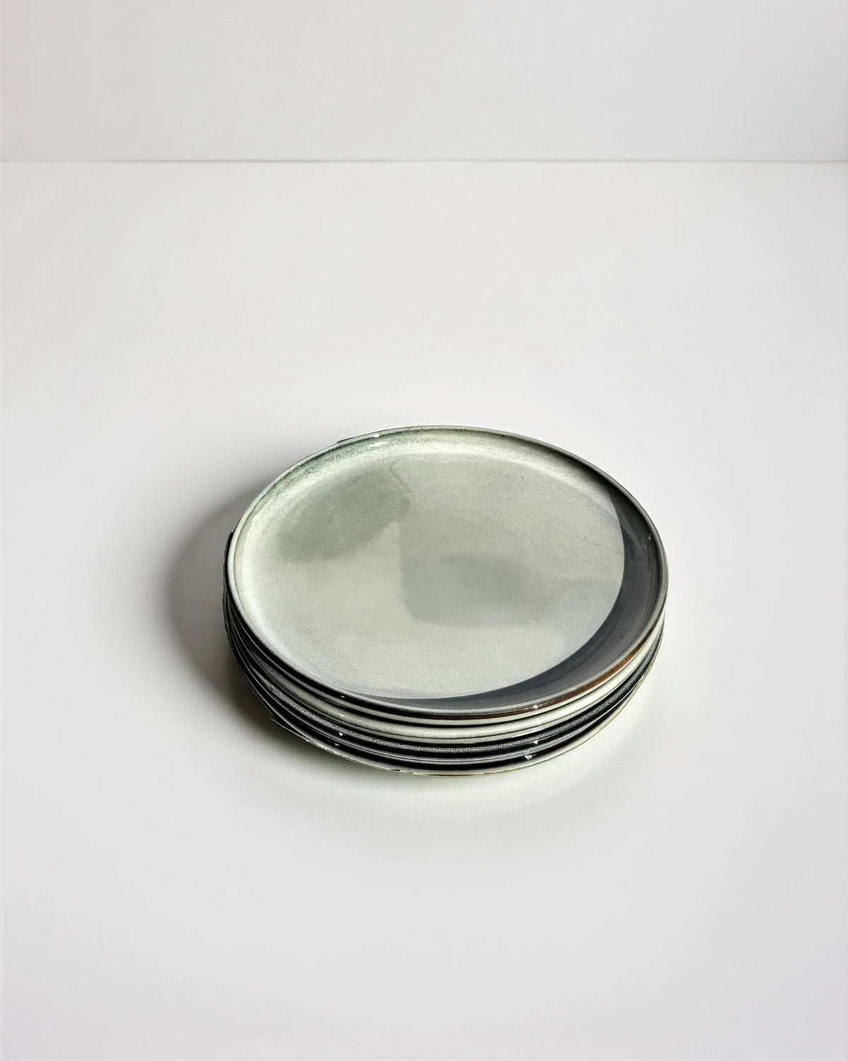Stack of six round metal plates with a pale gray glaze.