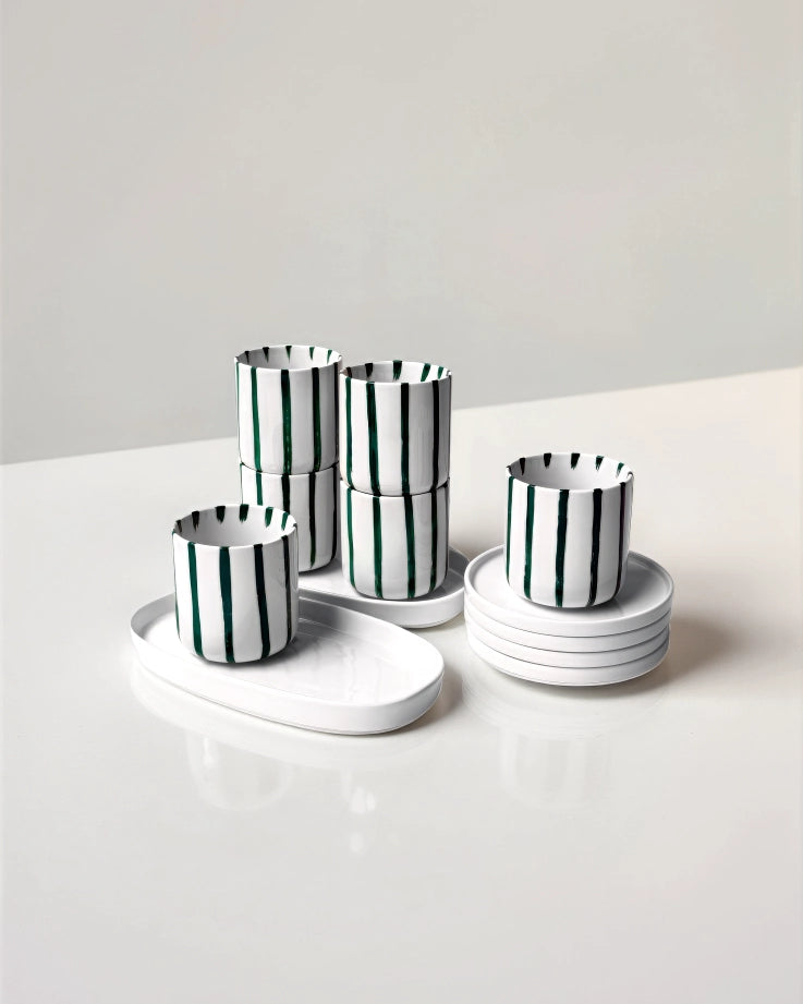 White cups with dark green vertical stripes stacked with matching white saucers from Karl Kaffeemomente Set.