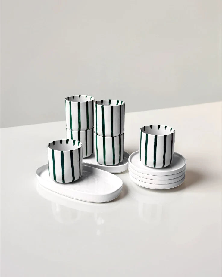 White cups with dark green vertical stripes stacked with matching white saucers from Karl Kaffeemomente Set.