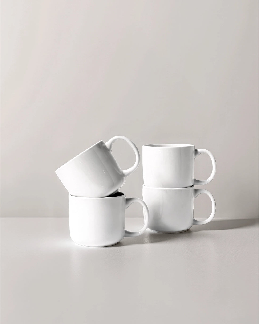 Set of four white Vela Alba mugs with a saucer on a pale background.