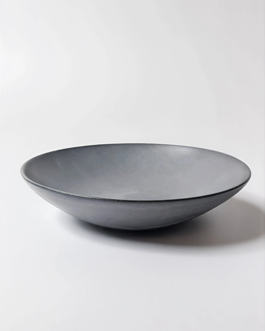 Grey shallow pasta plate with a smooth curved rim on a white background