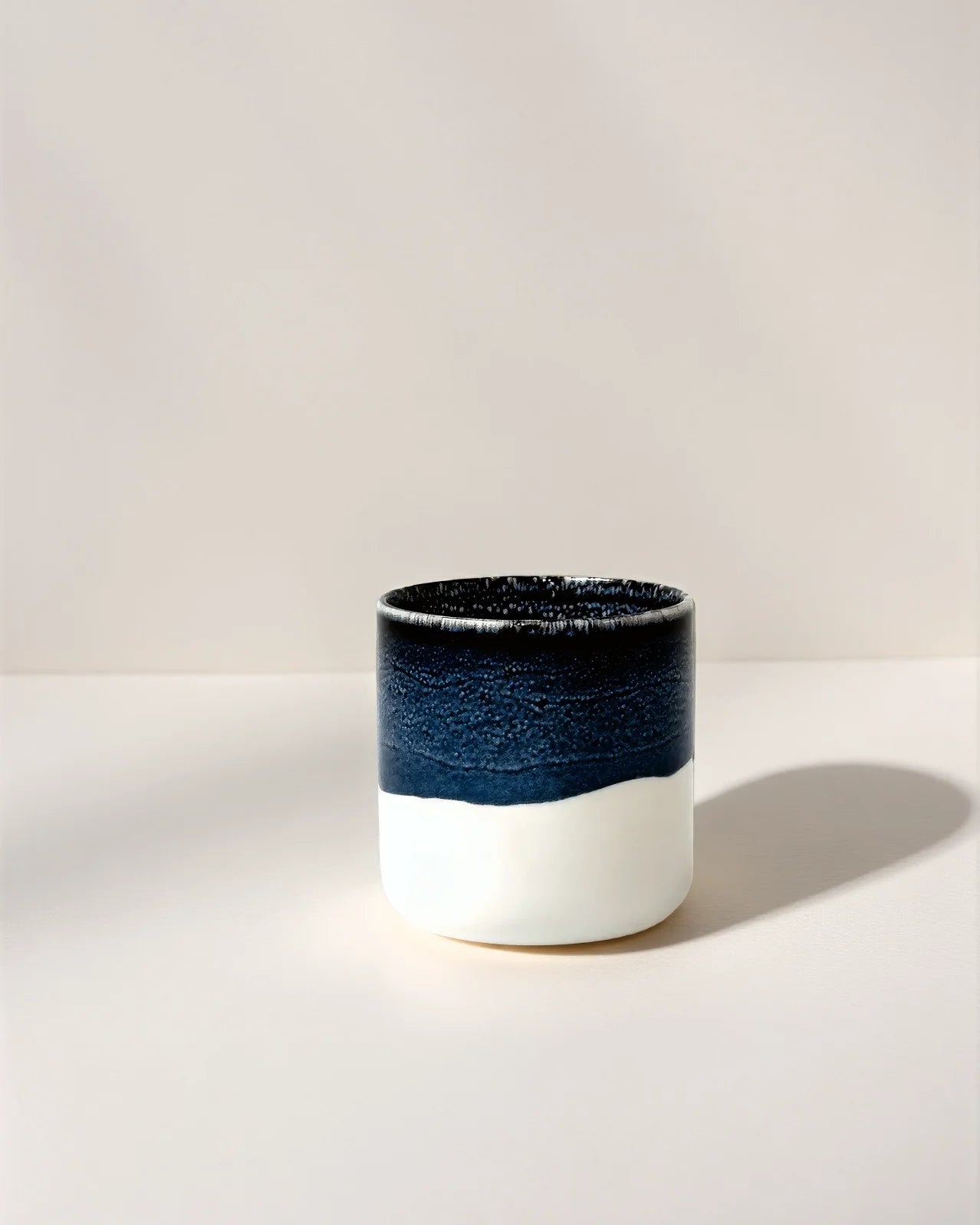 Close up of a blue and white banded ceramic cup on a pale background.