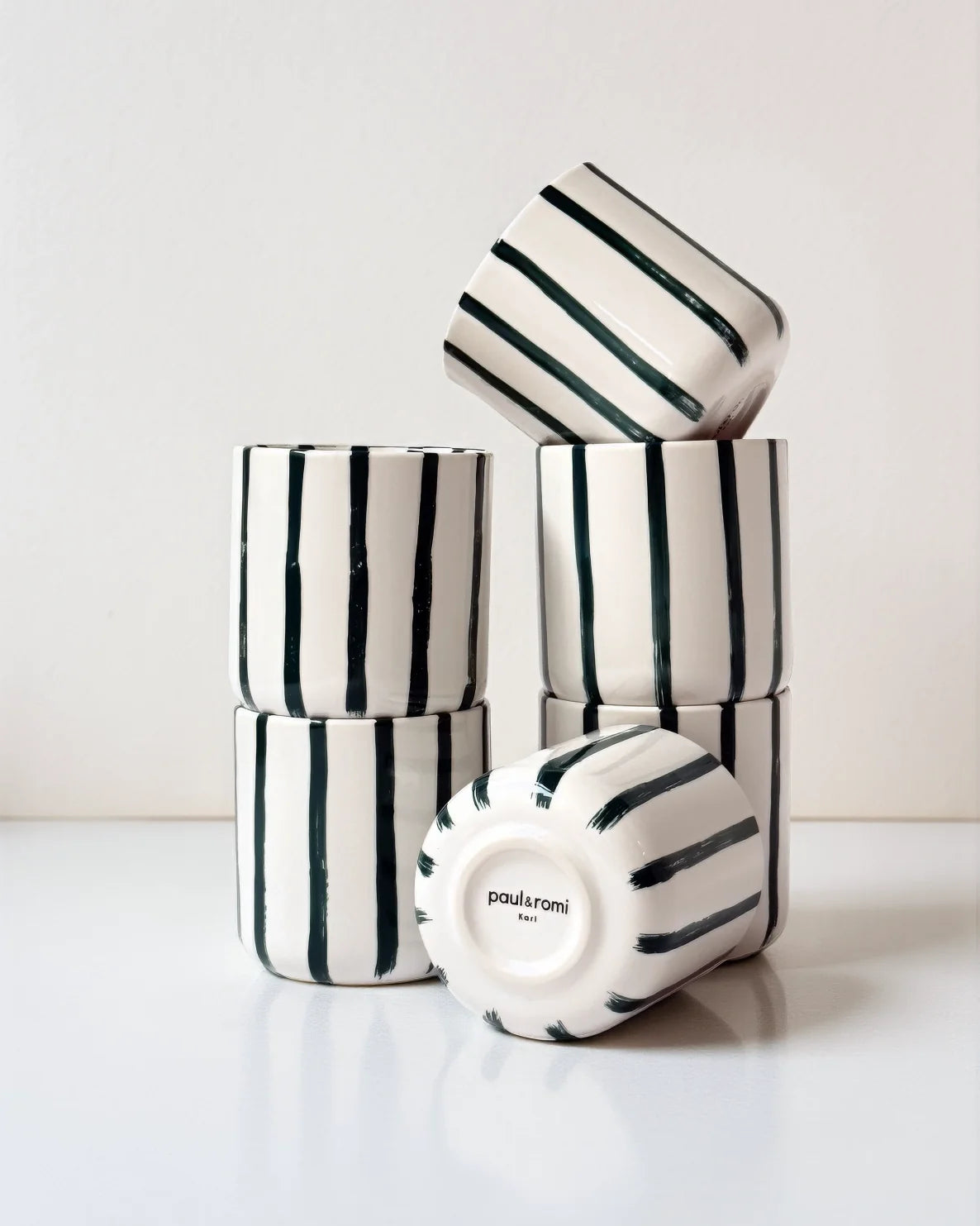 White cups with bold vertical stripes stacked, one cup tilted to the side showing paul & romi Karl on the base.