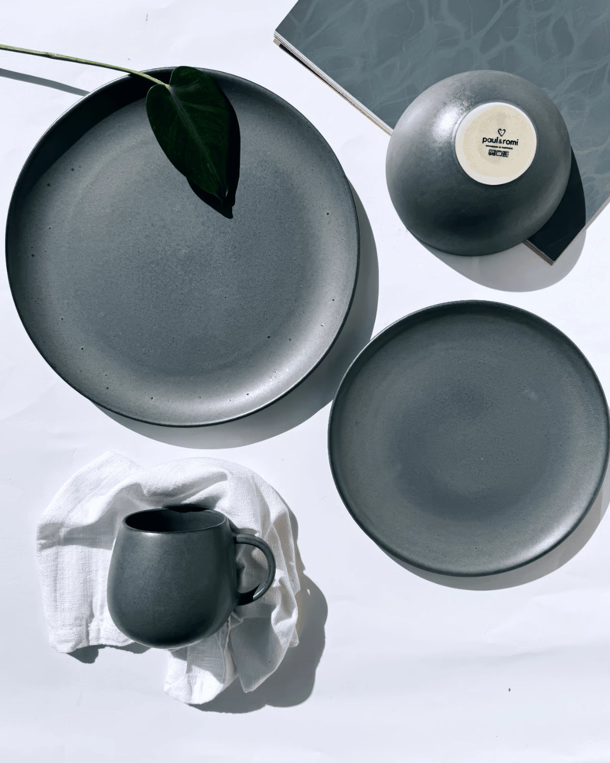 Matte grey dessert plates arranged on a white surface with a green leaf.