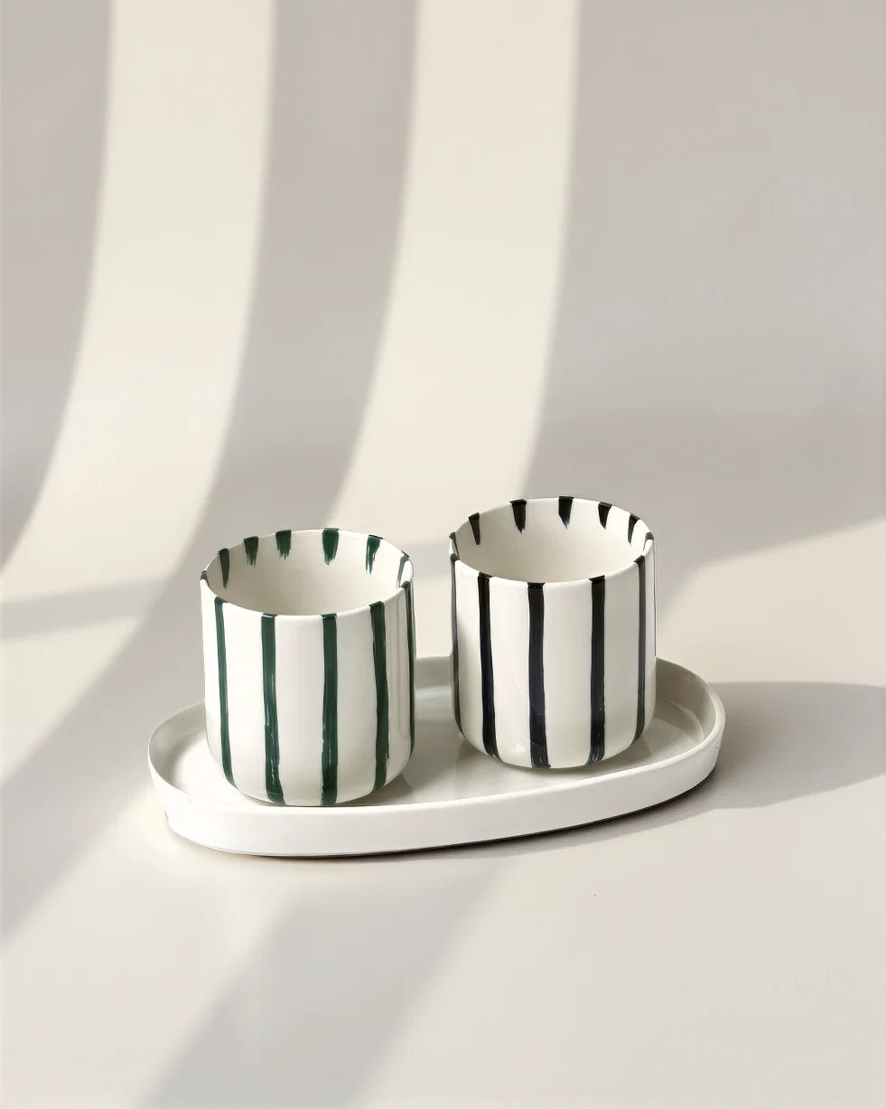 Two striped ceramic coffee cups with vertical green and black stripes on a white oval tray.