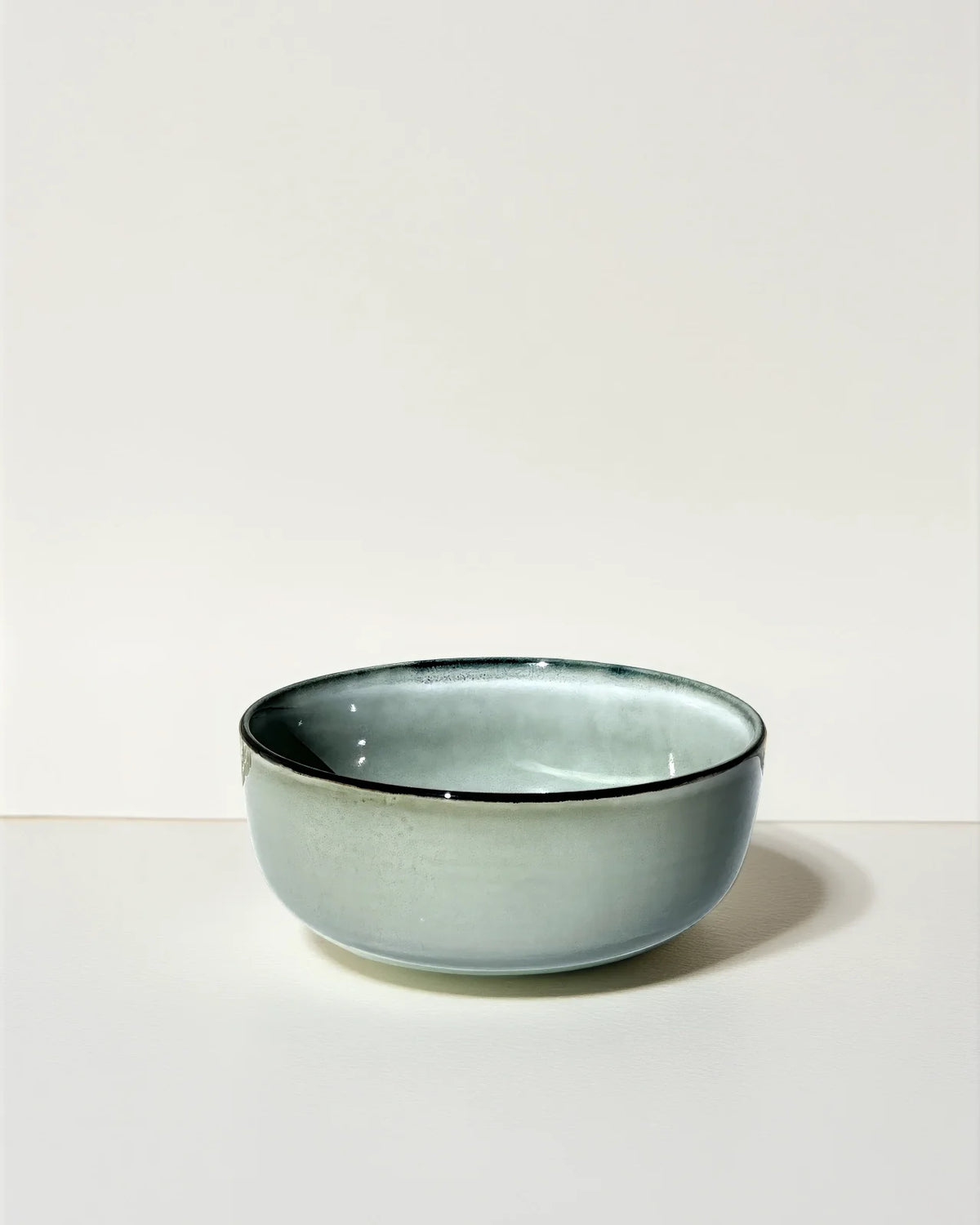 Pale blue gray ceramic bowl displayed on a light neutral backdrop in a studio setting