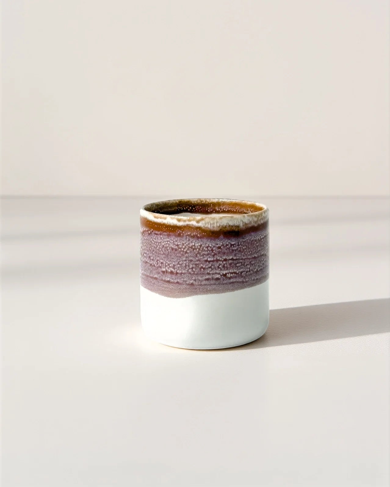 Elda Kaffeemomente Becher mit braunvioletter Glasur und weißer Basis auf heller Oberfläche
