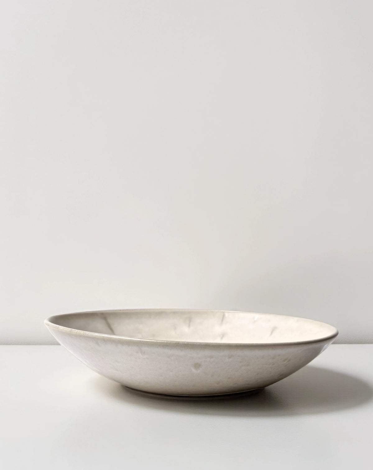 Bom Dia marbleized ceramic pasta bowl on a pale backdrop.