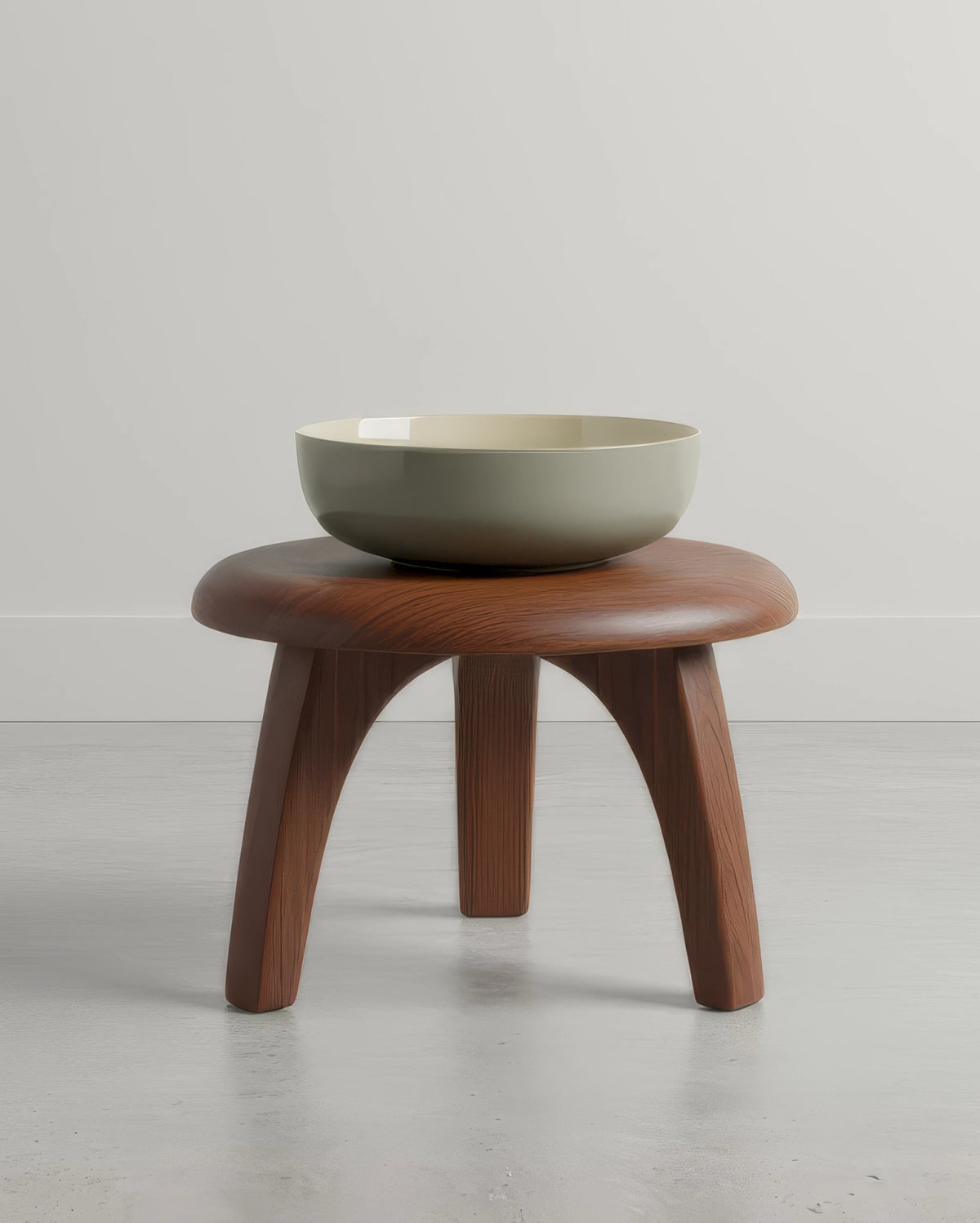 Large muted olive green ceramic bowl perched on a round wooden stool.